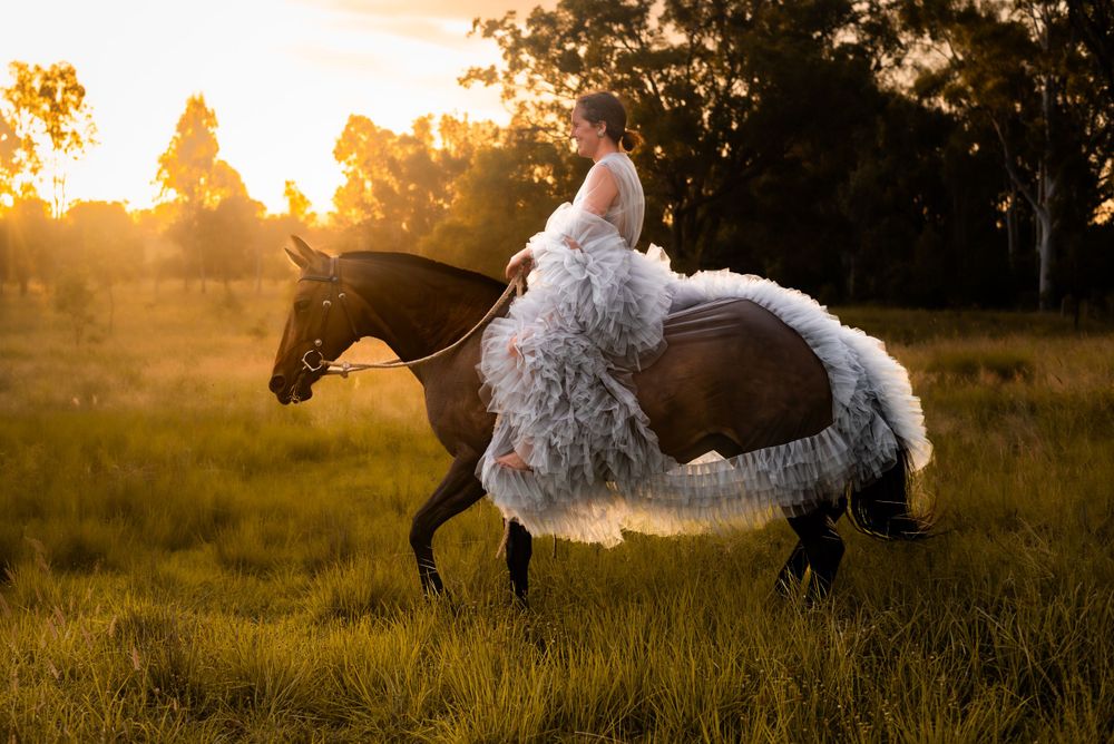 A horse and rider in a flowing white dress silhouetted against a golden sunset in a field.