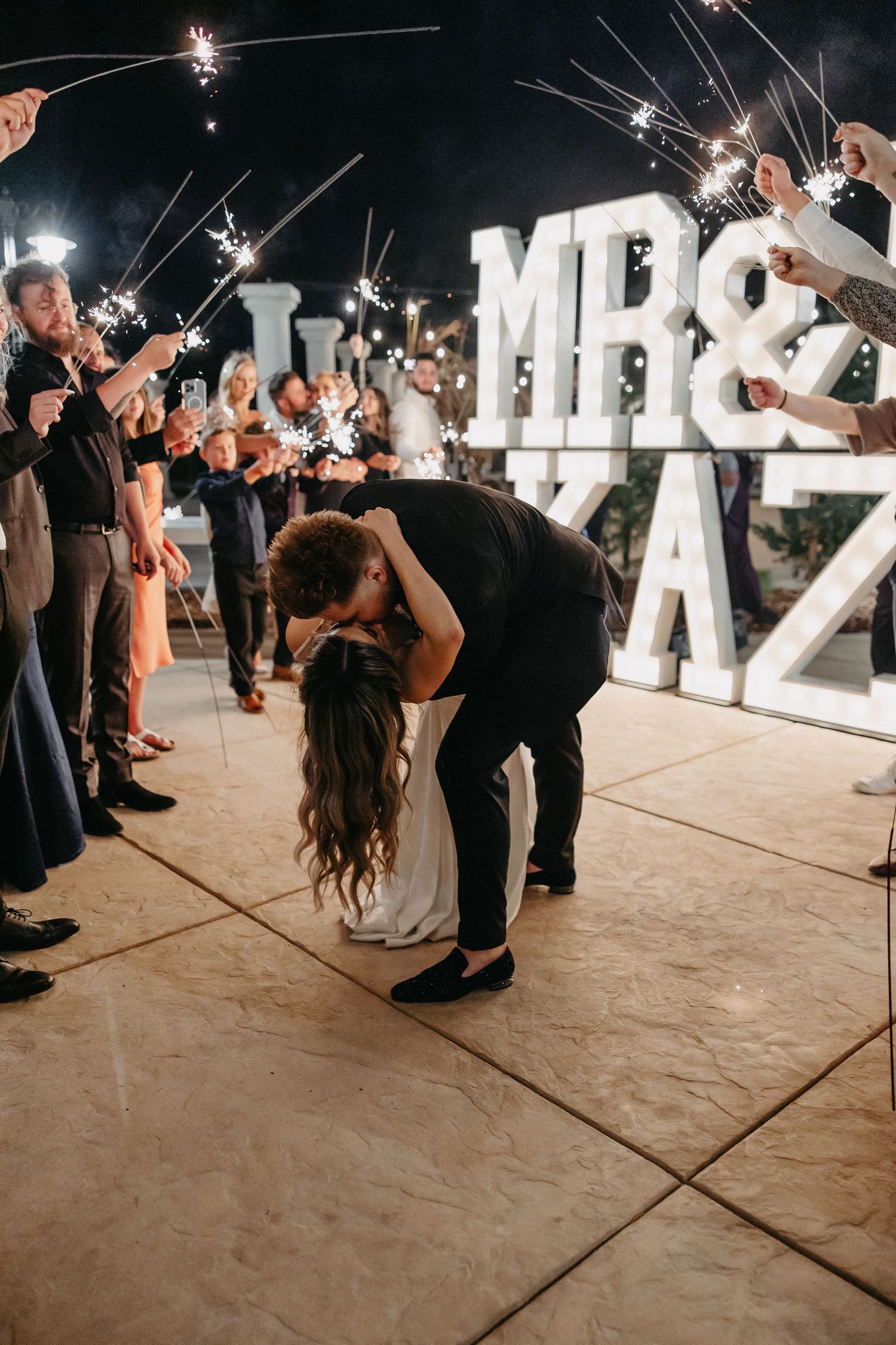 A dramatic dip during sparkler exit with guests lining the walkway at nighttime wedding celebration.