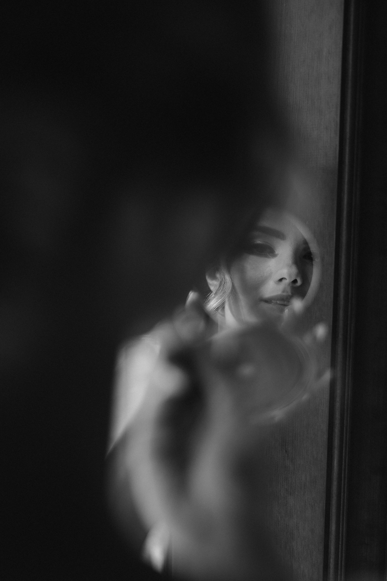 Artistic black and white portrait of bride reflected in shadowy mirror.