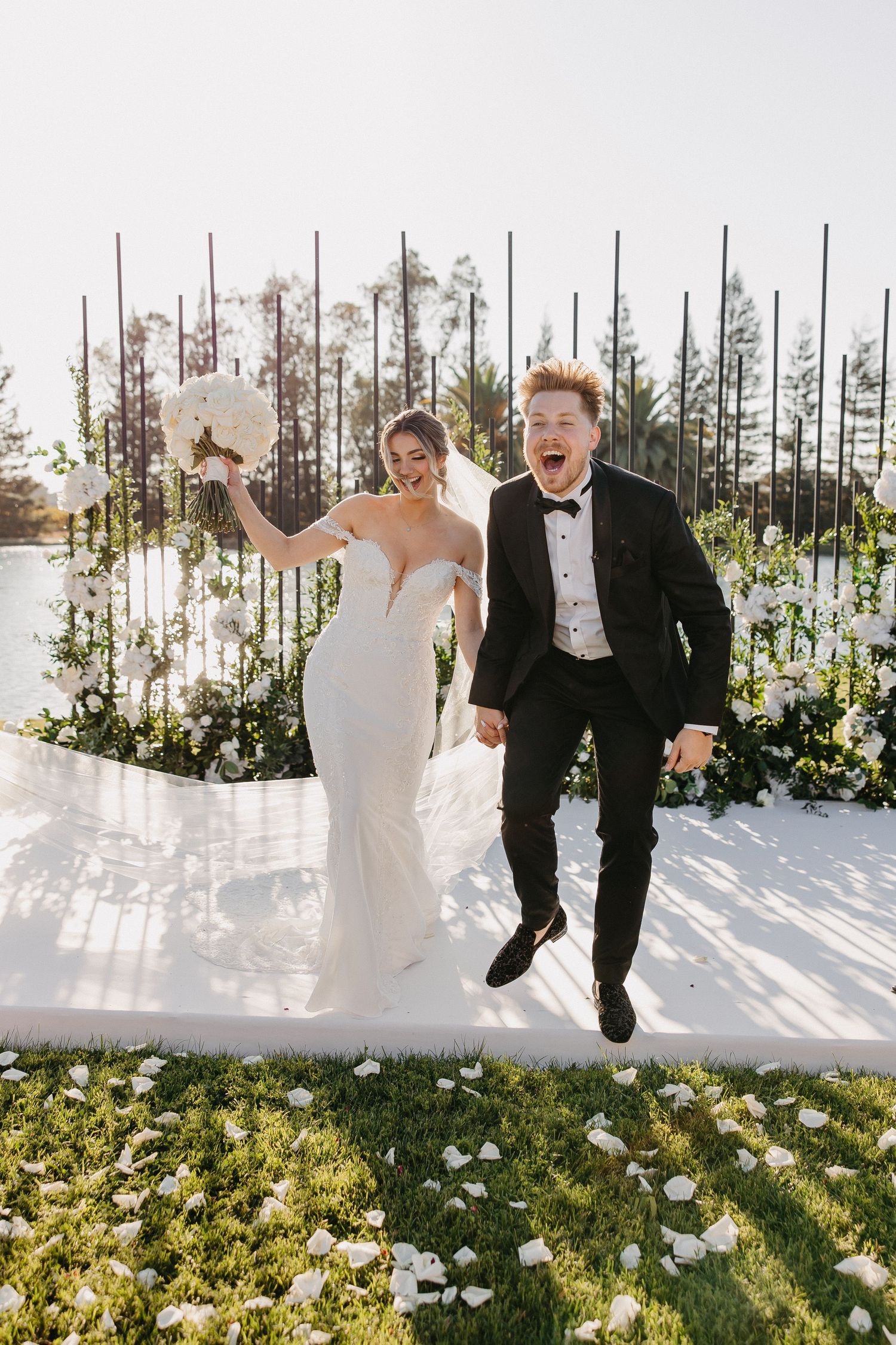 Newlyweds jumping with joy during their outdoor wedding celebration among floral decorations.
