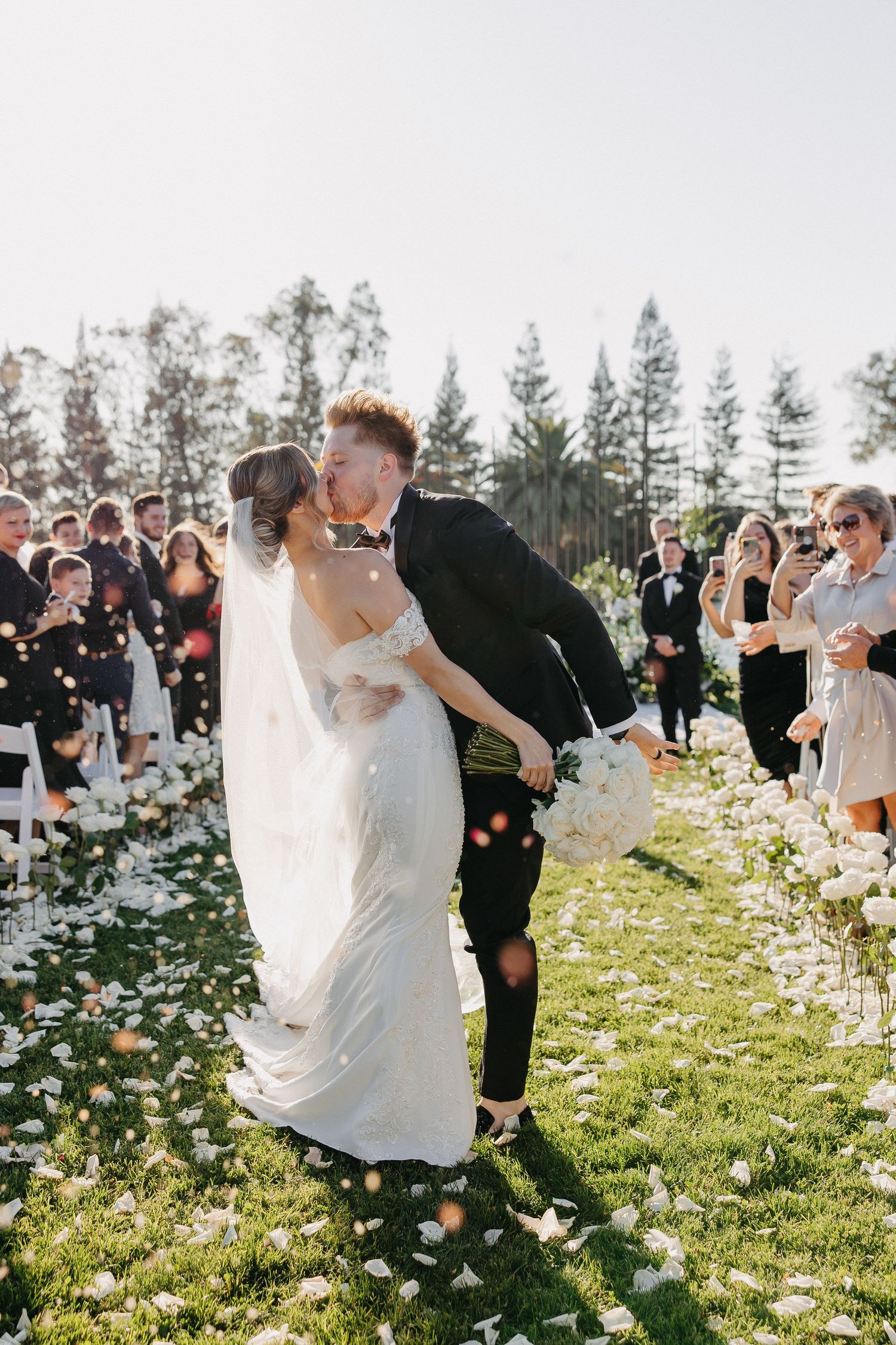 Couple shares intimate moment during wedding recessional as guests shower them with confetti.