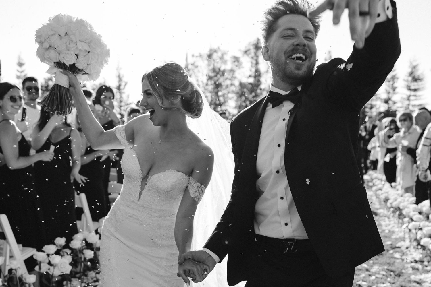 Black and white photo of newlyweds celebrating with exuberant joy during wedding recessional.