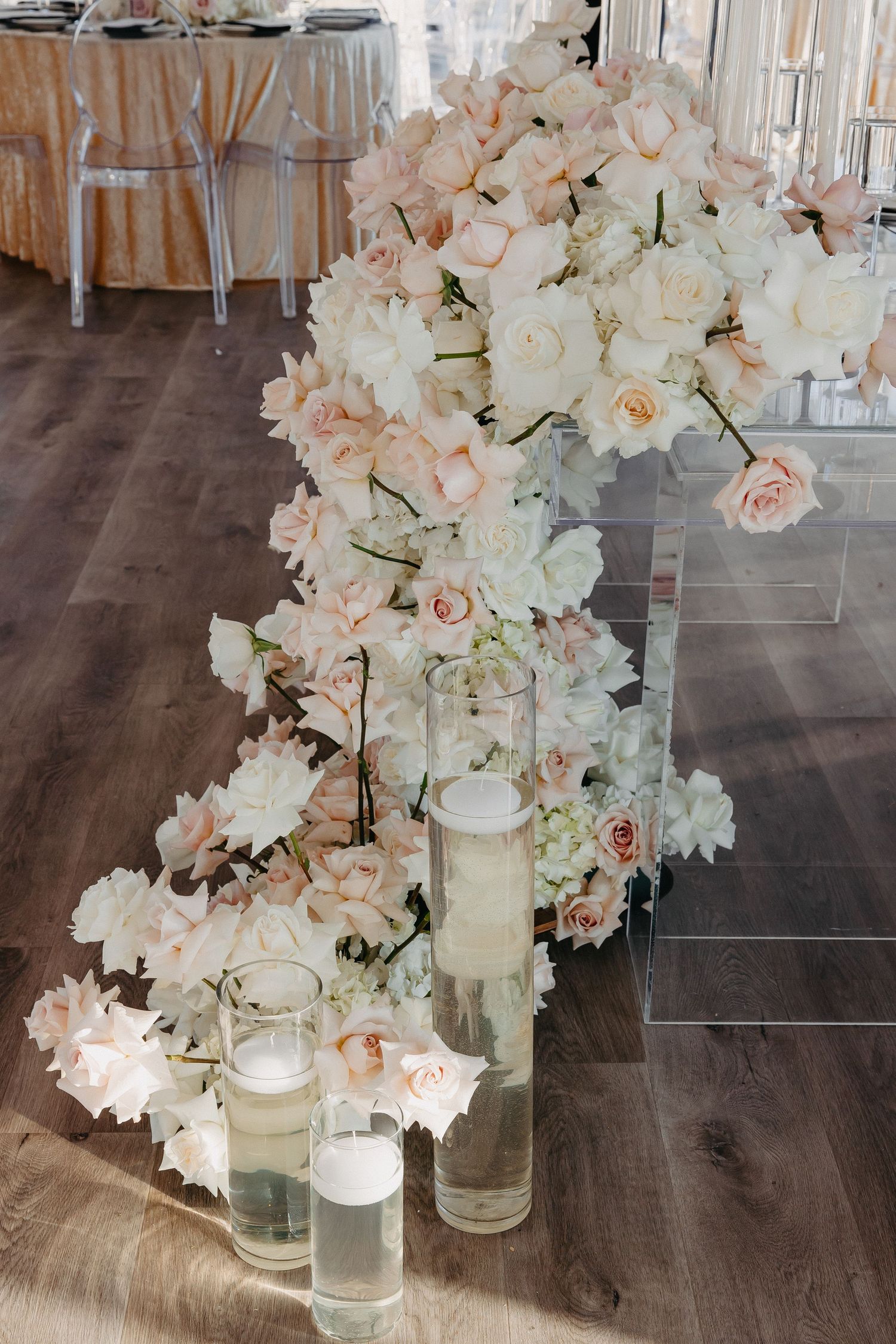 Romantic floral arrangement with blush roses and candles displayed along wooden floor.