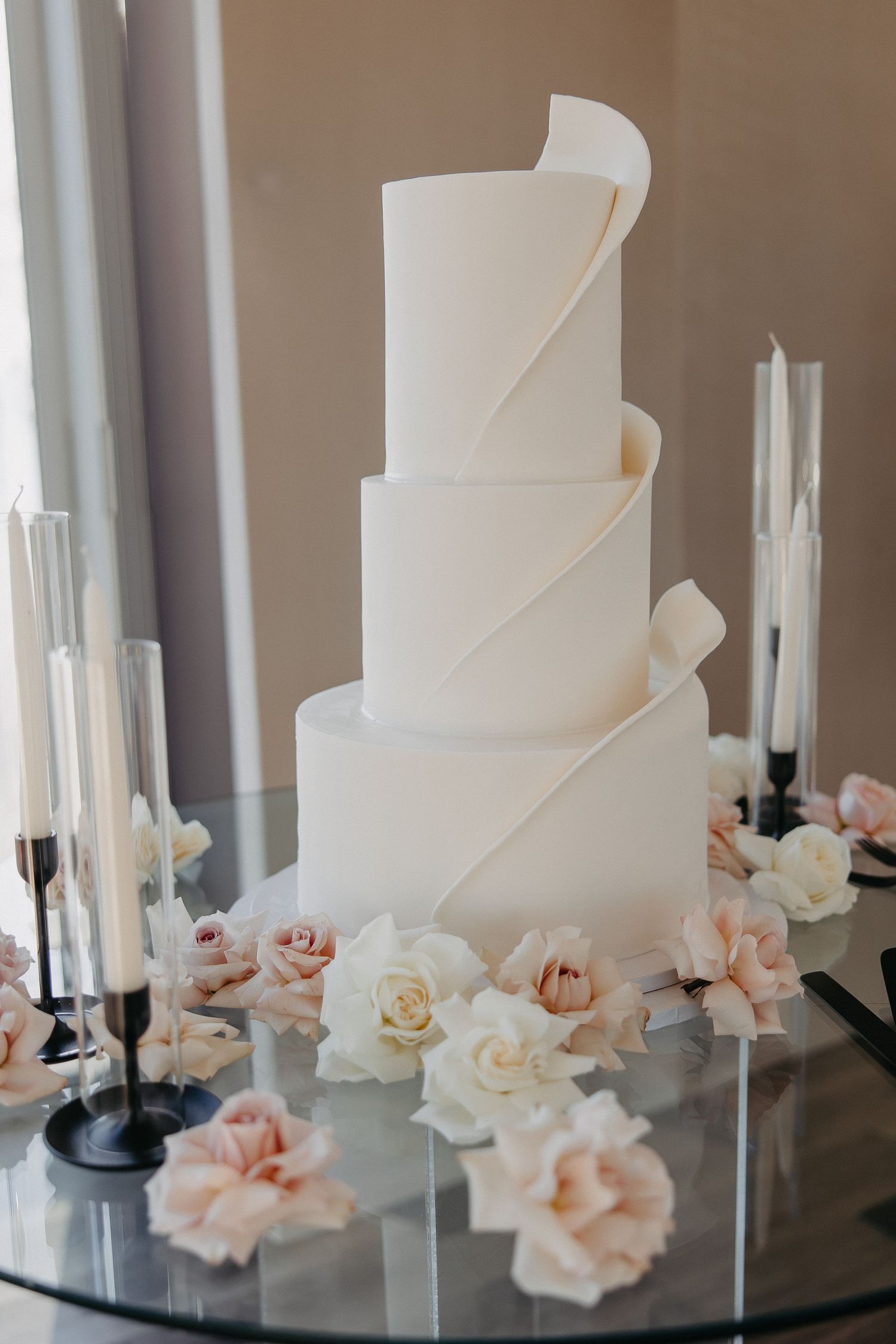 Modern white wedding cake with geometric details and blush roses on mirrored stand.