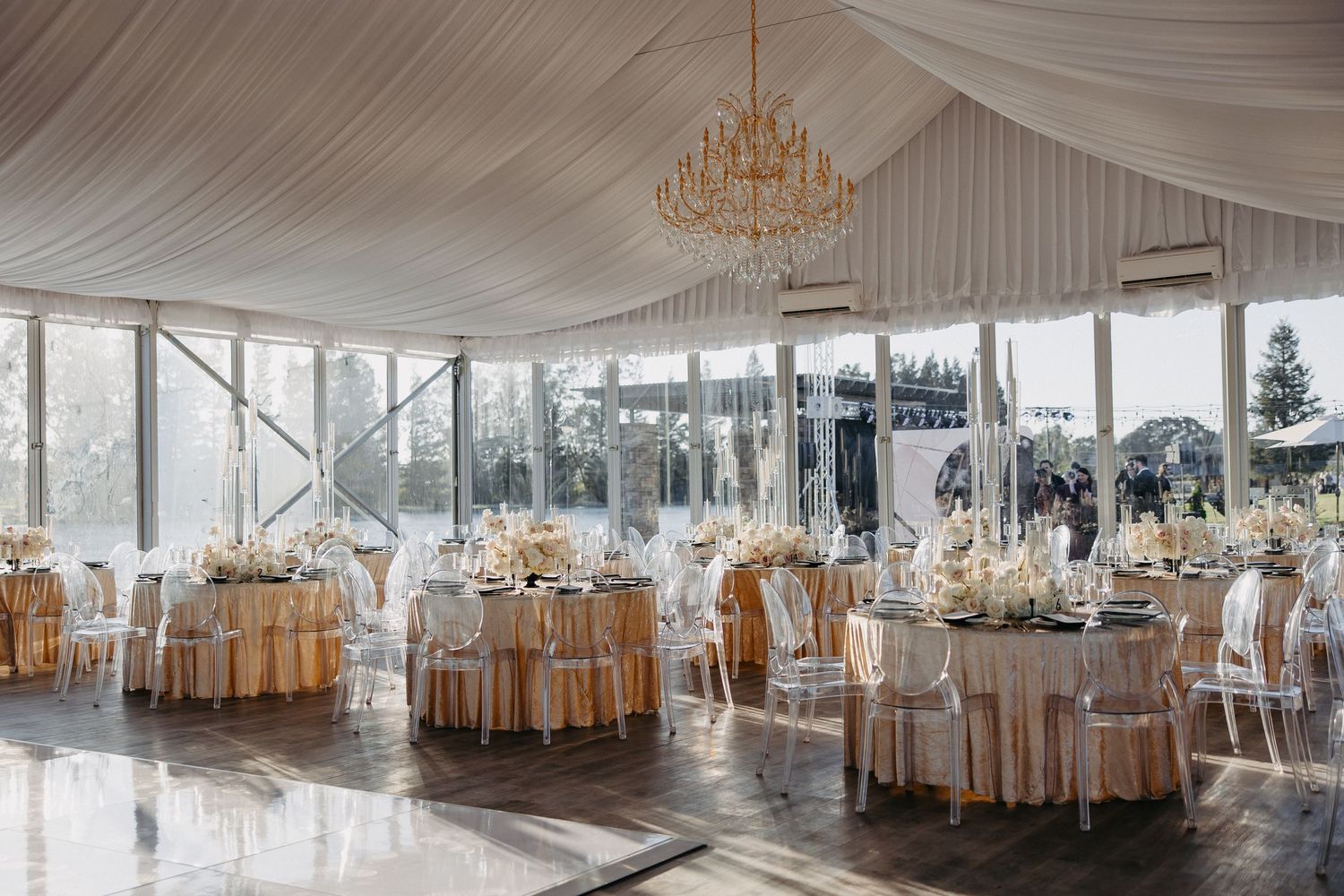 Elegant wedding reception venue with draped ceiling, chandeliers and cream-colored table settings.