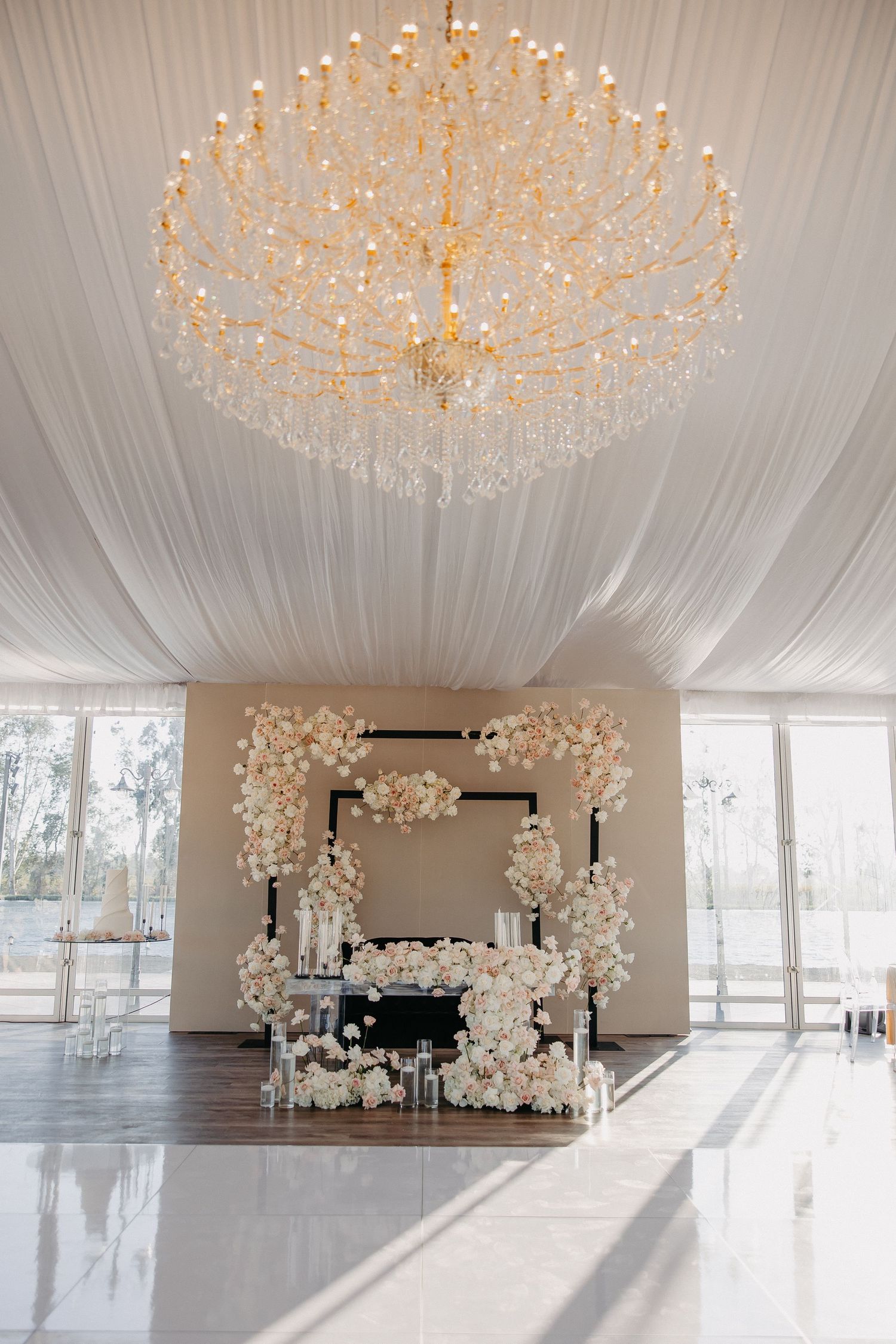 Grand crystal chandelier above white floral installation in elegant wedding venue.