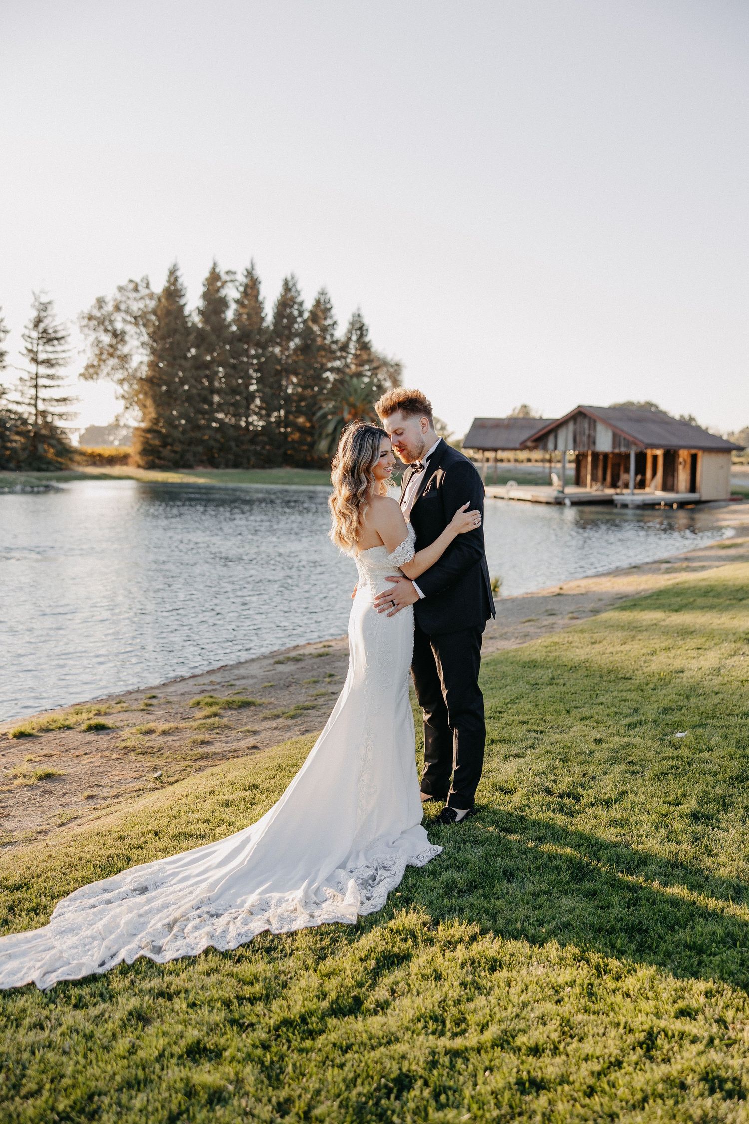 Romantic lakeside wedding portrait with water and pine trees in background.