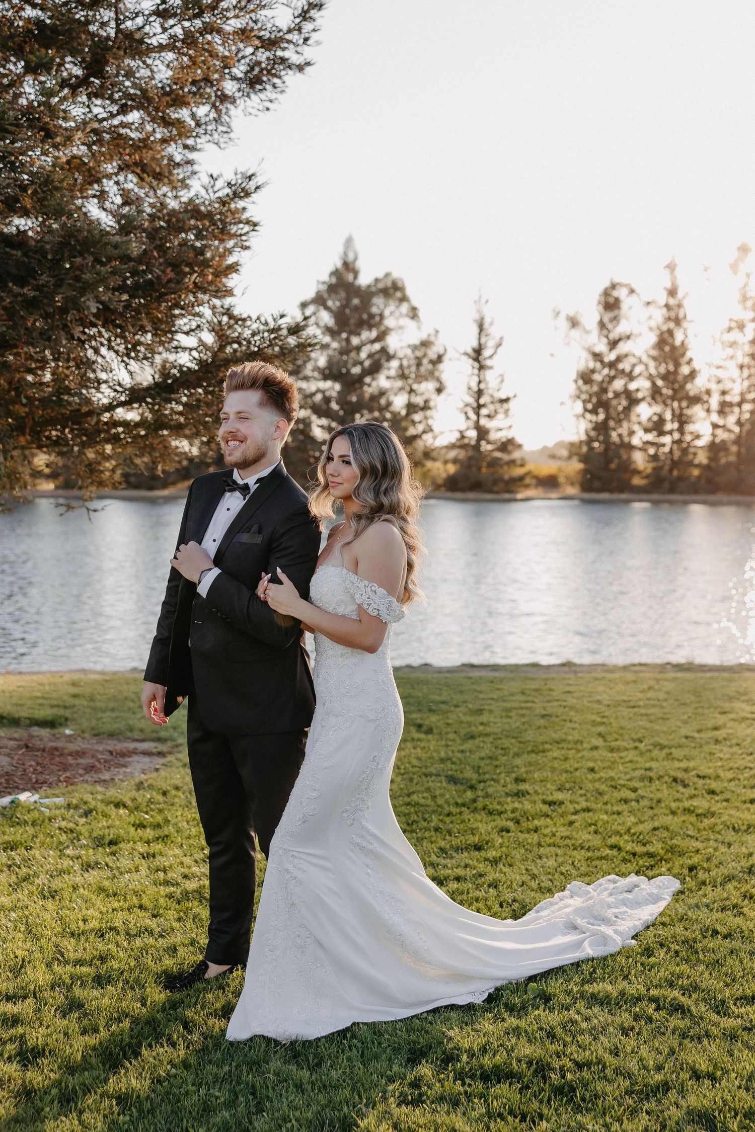 Couple laughs together during lakeside wedding photoshoot at golden hour.