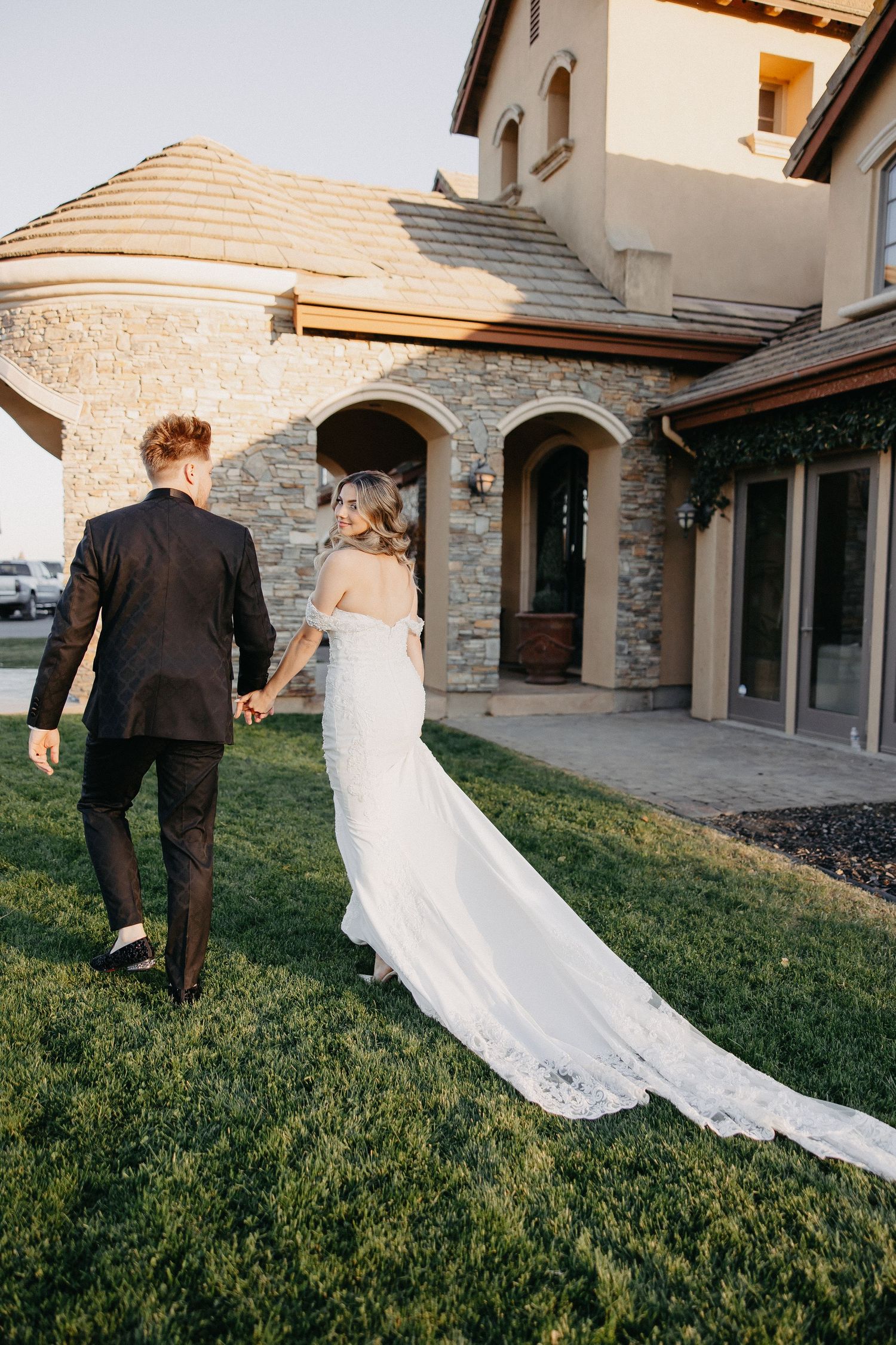 Couple walking towards stone mansion entrance with flowing wedding dress train.