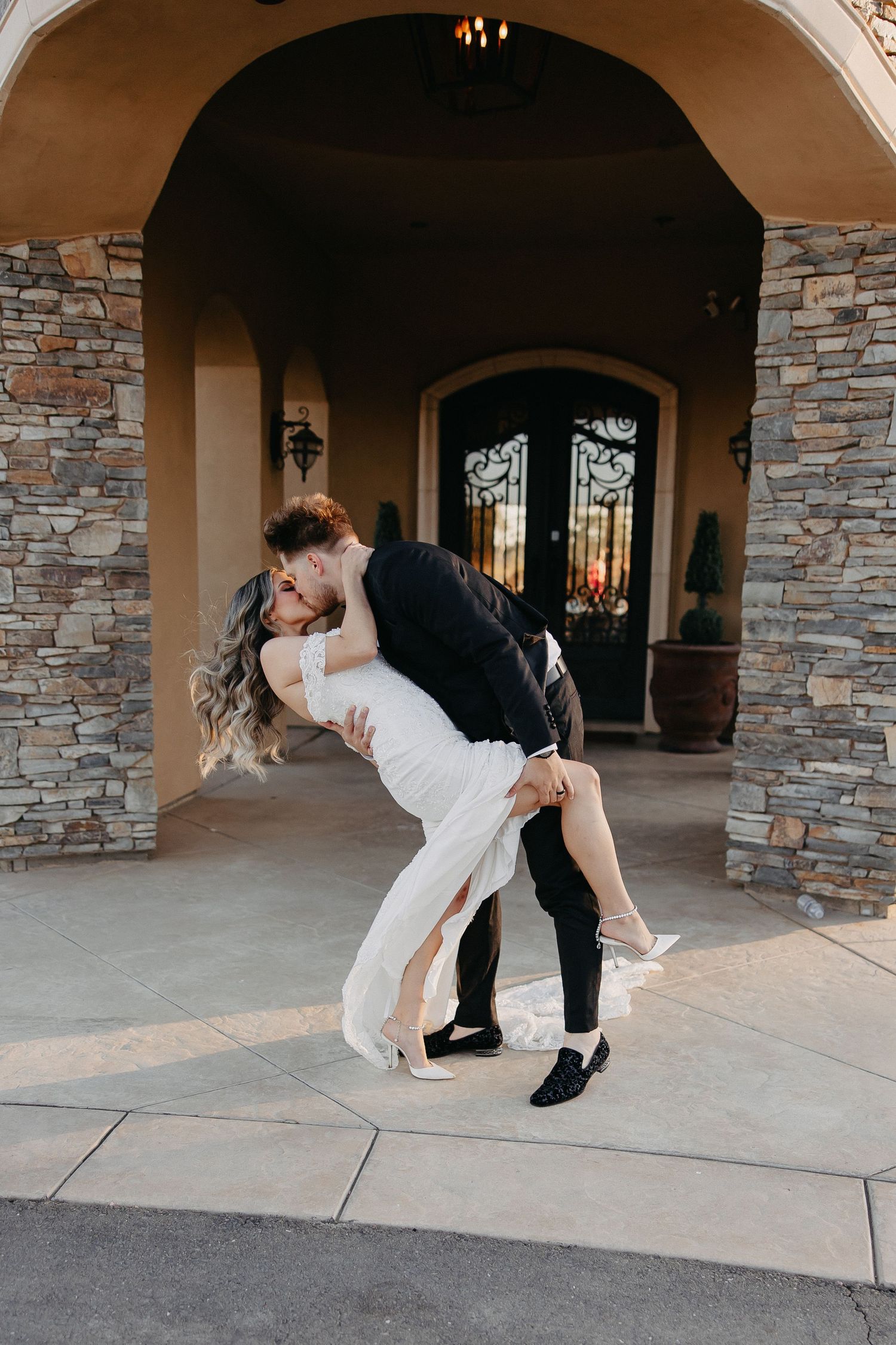 Romantic dip pose under stone archway entrance during wedding photoshoot.
