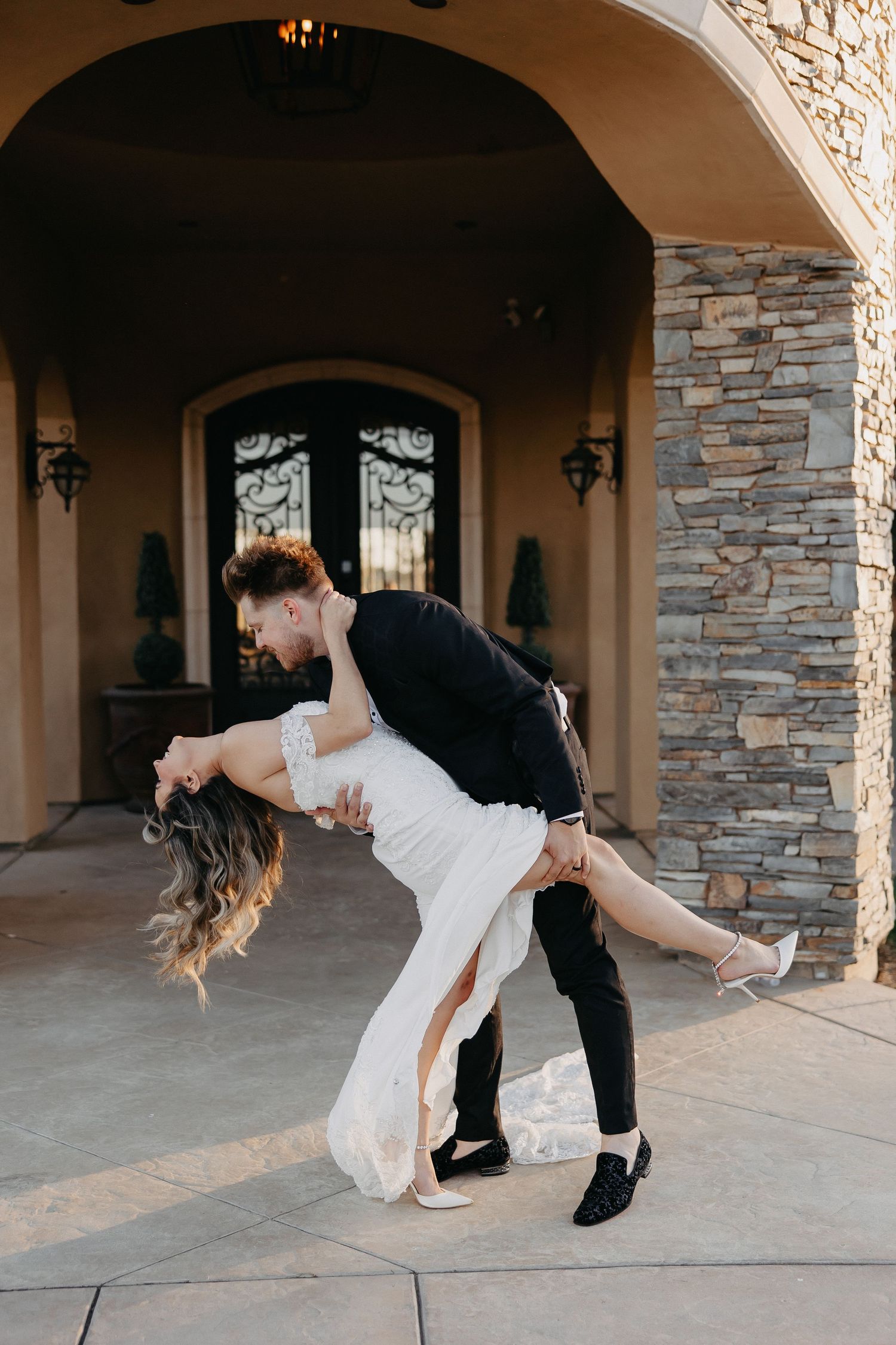 A romantic dip pose in front of a stone archway entrance during wedding photoshoot.