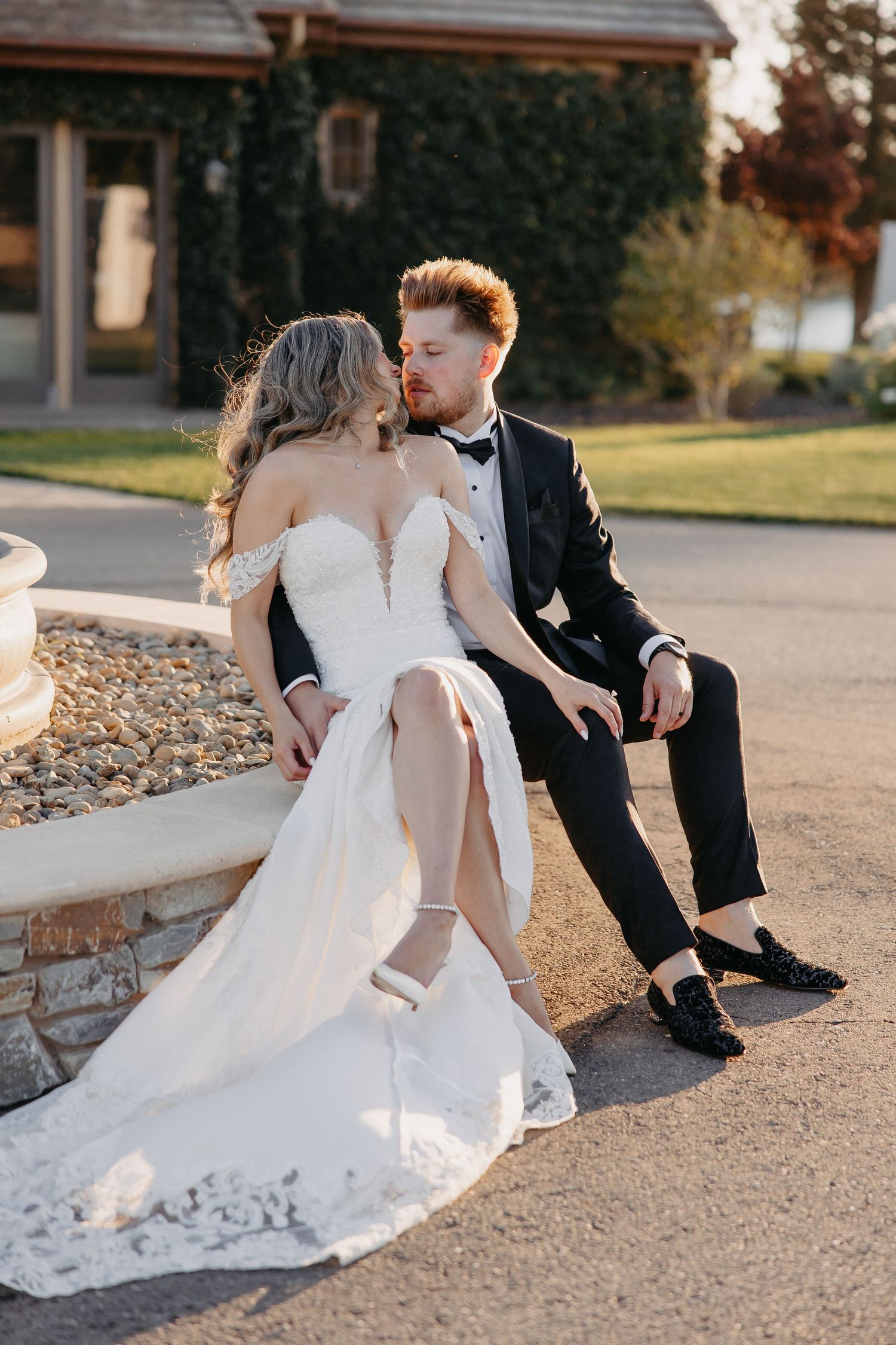 A romantic wedding couple sits together on a stone wall during golden hour.