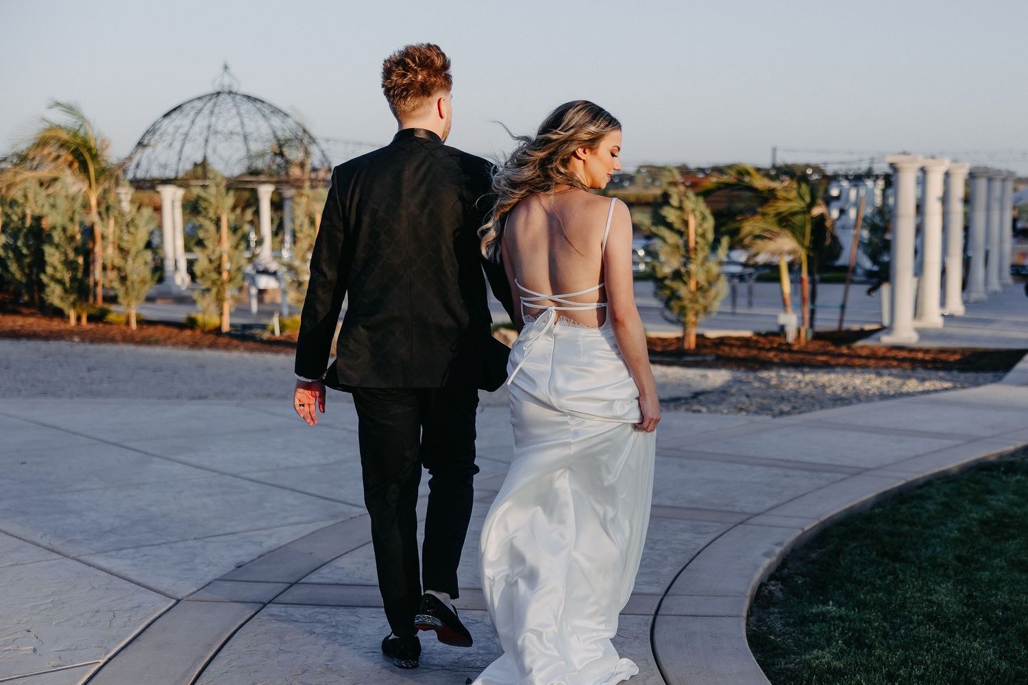 Couple walking away on stone path with wedding gazebo and palm trees in background.