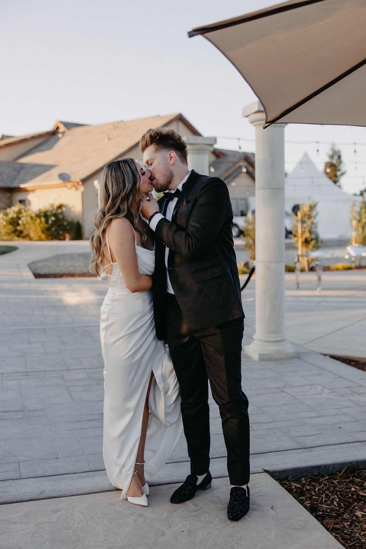 A romantic wedding couple shares an intimate moment under a covered patio at sunset.