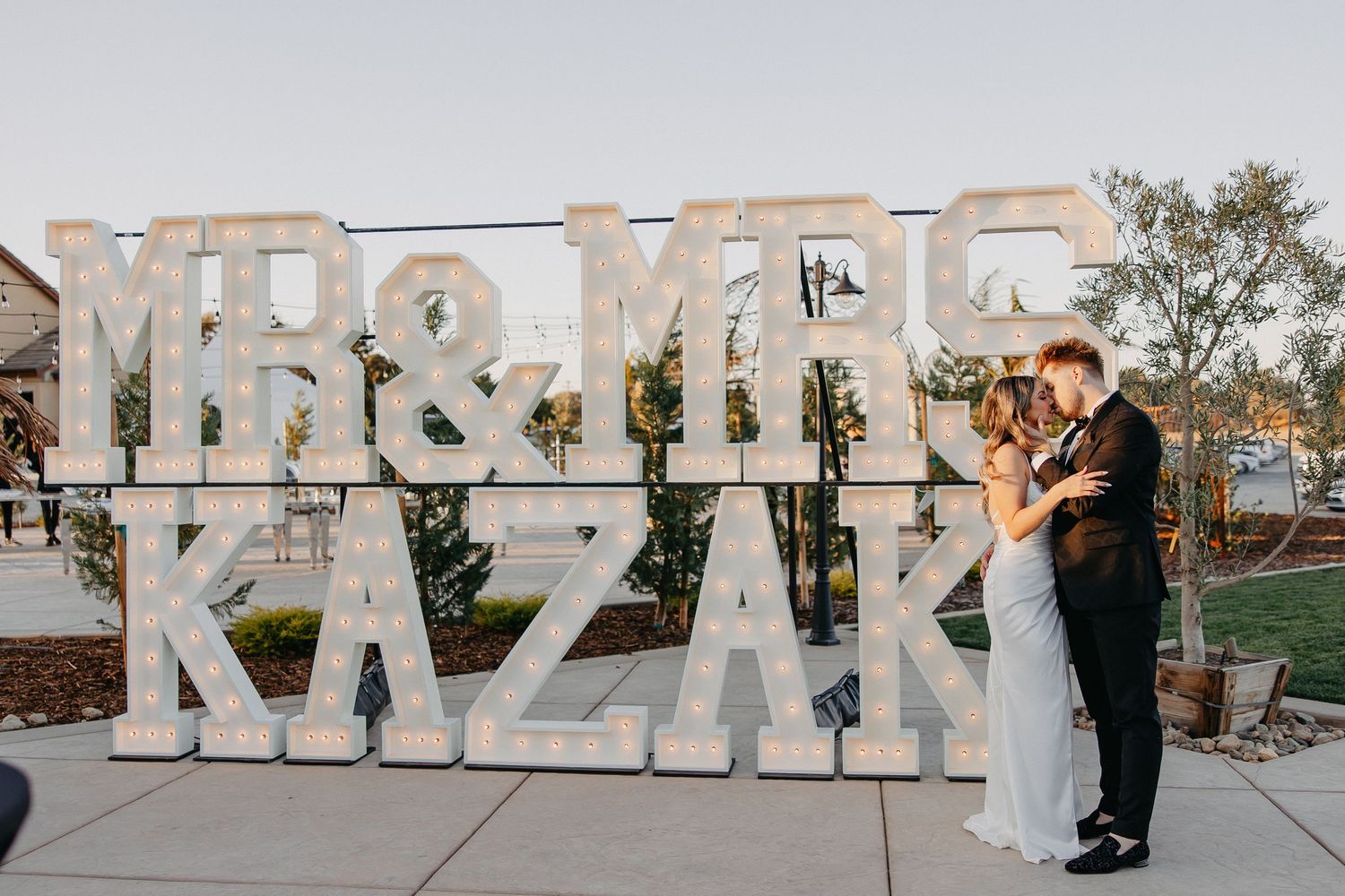 A wedding couple poses in front of large decorative letters spelling 'MR & MRS' at their reception venue.