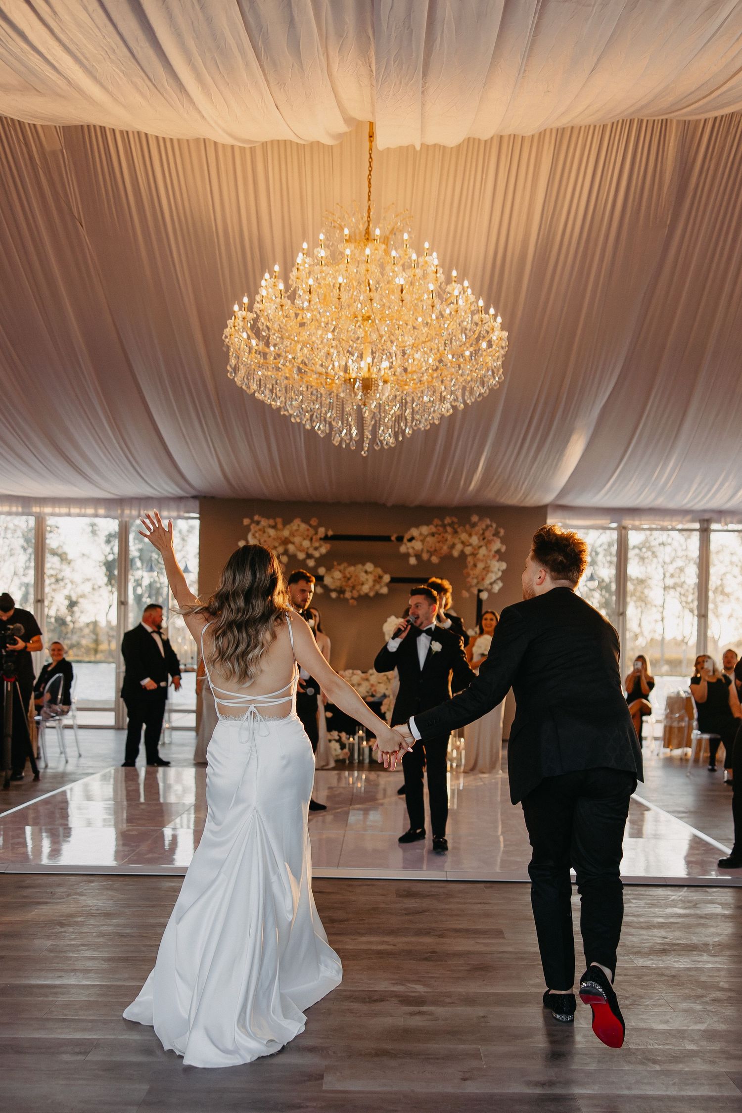 A wedding reception ballroom decorated with white draping and an ornate crystal chandelier.