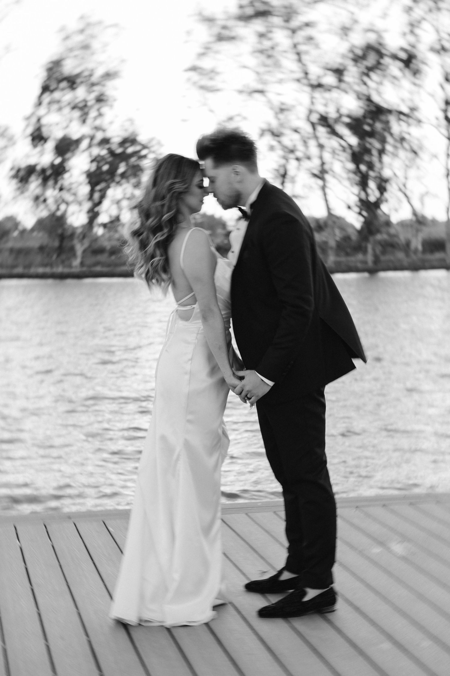 Black and white romantic photo of a couple sharing an intimate moment on a dock by the water.