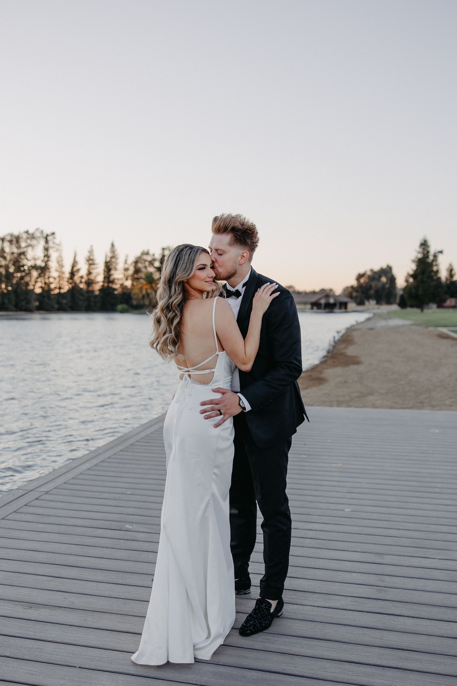 A romantic sunset photoshoot of a couple embracing on a waterfront boardwalk.