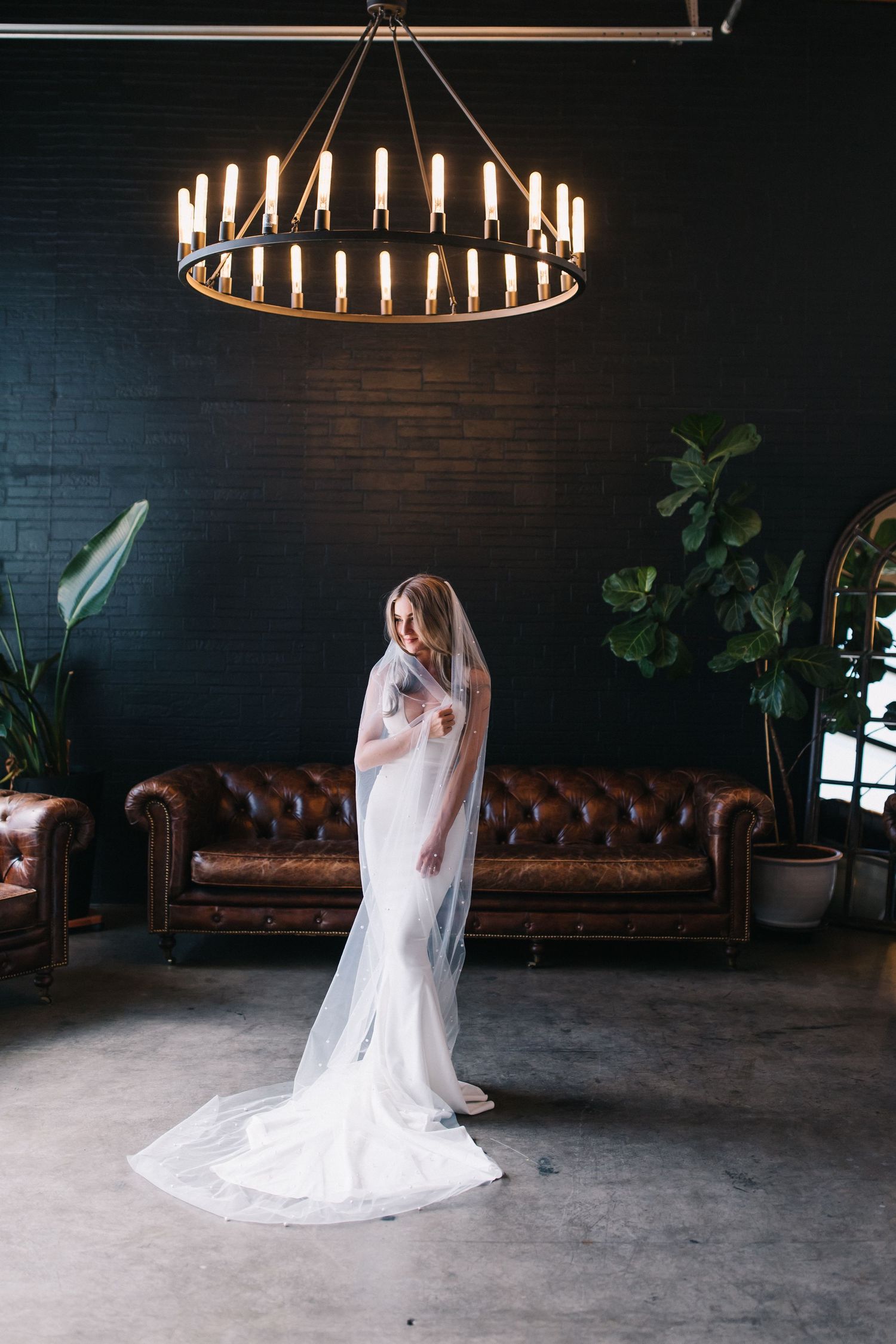 Bridal portrait under a circular chandelier with leather sofa and dark walls in the background.
