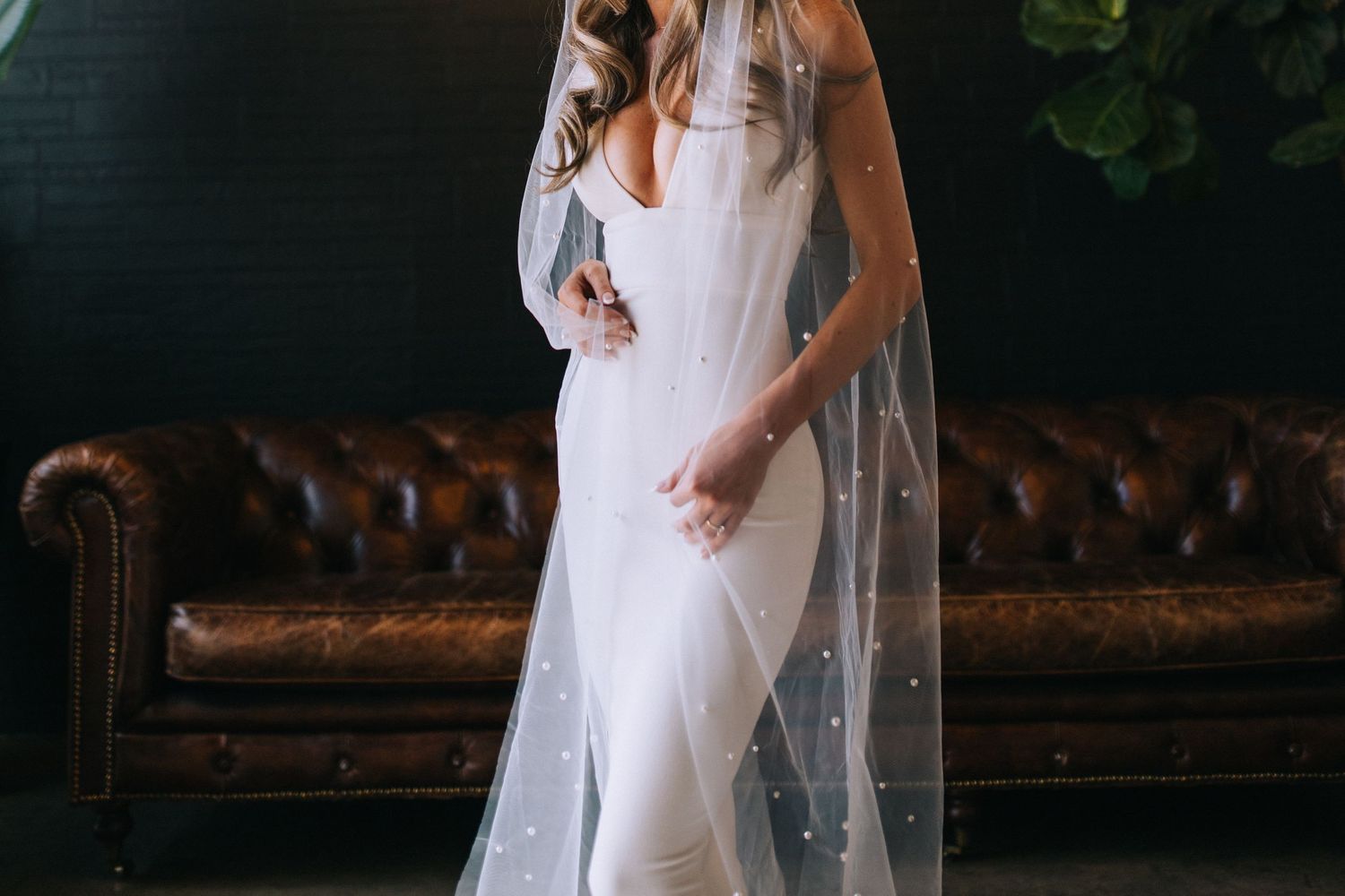 Elegant bridal portrait featuring a fitted white gown with sparkle veil against dark interior.