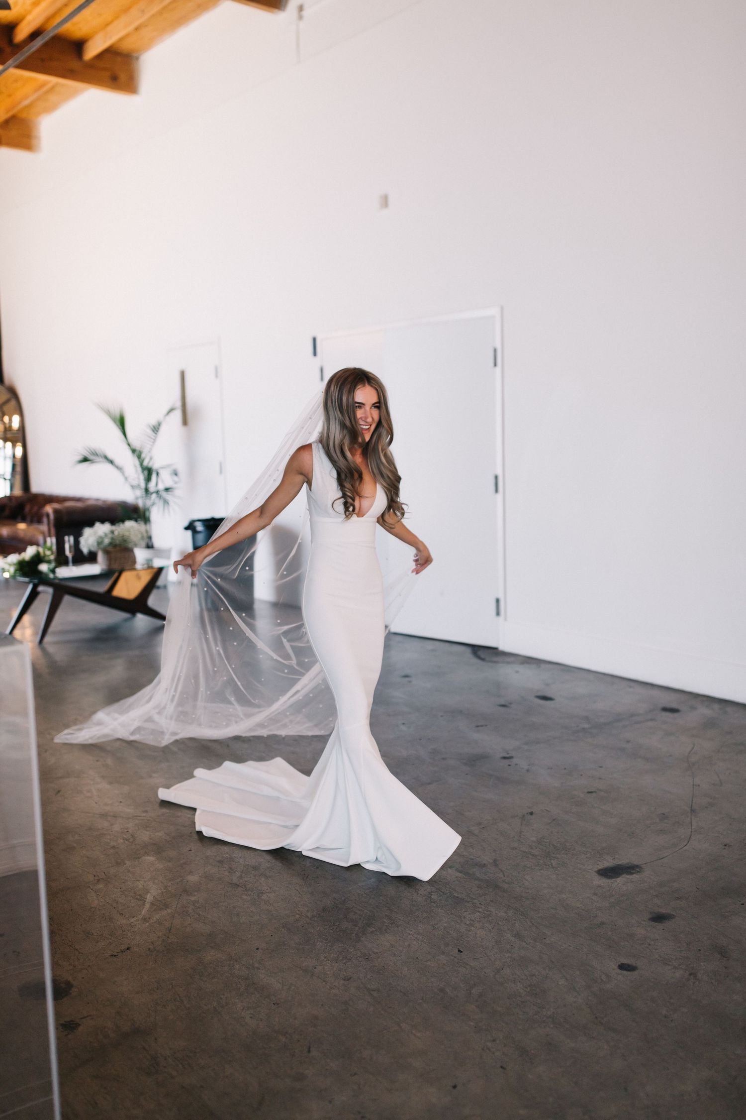 Bride twirling in a fitted mermaid wedding dress with flowing veil in an industrial space.
