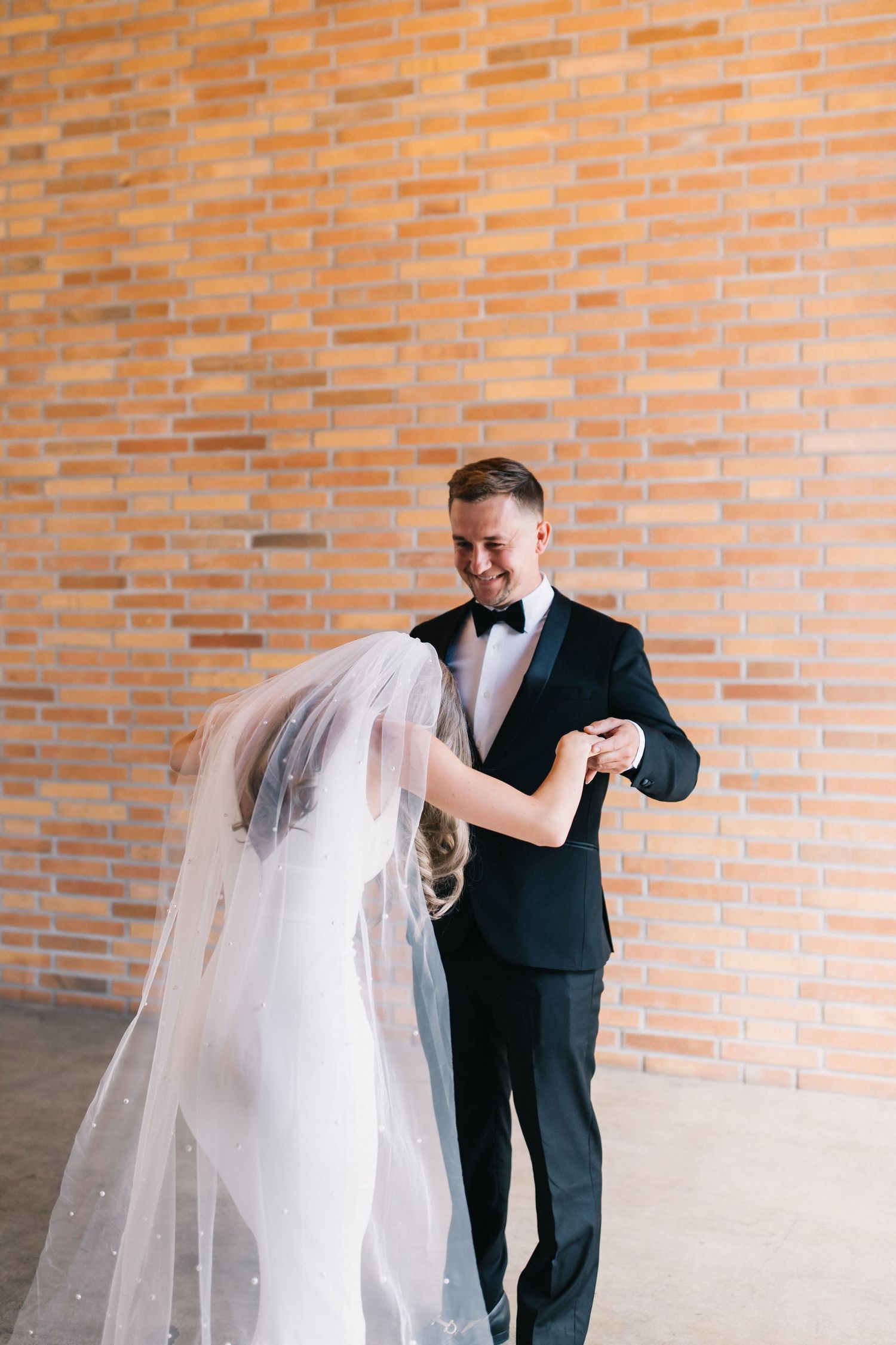 A wedding couple shares their first dance against a rustic brick wall backdrop.