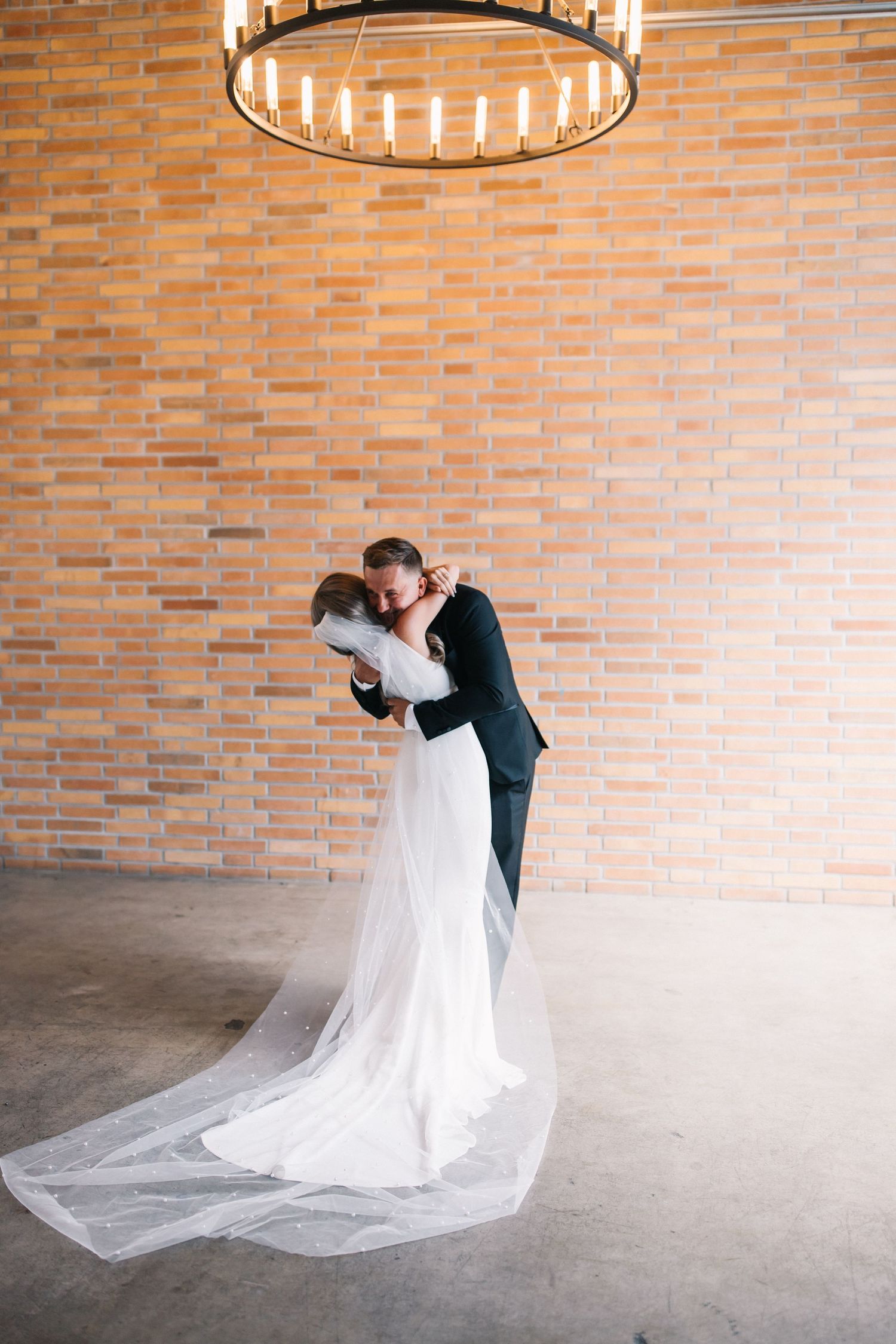 A romantic wedding moment under a circular chandelier with a flowing white veil.
