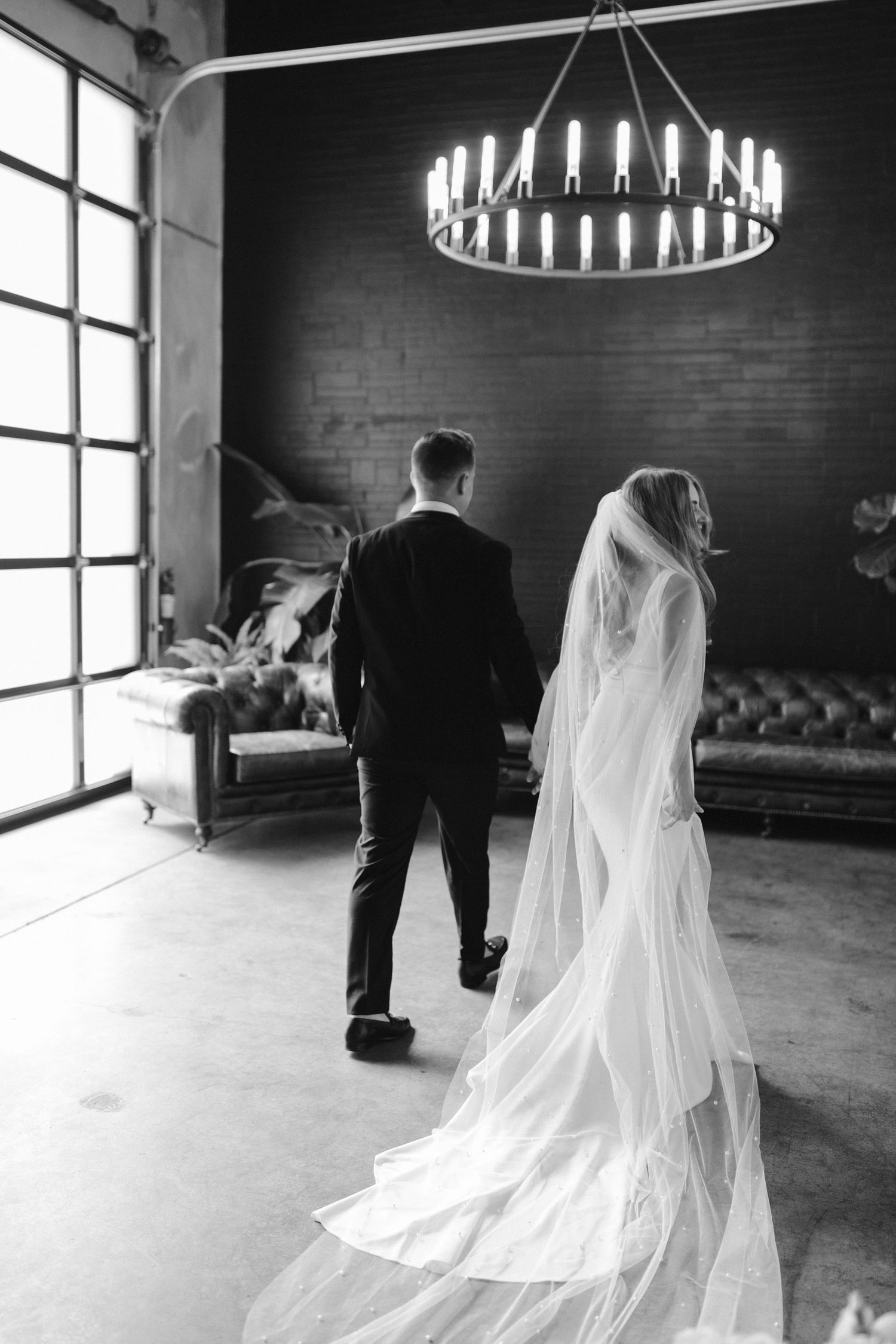 Black and white wedding photo with flowing veil and dramatic chandelier lighting.