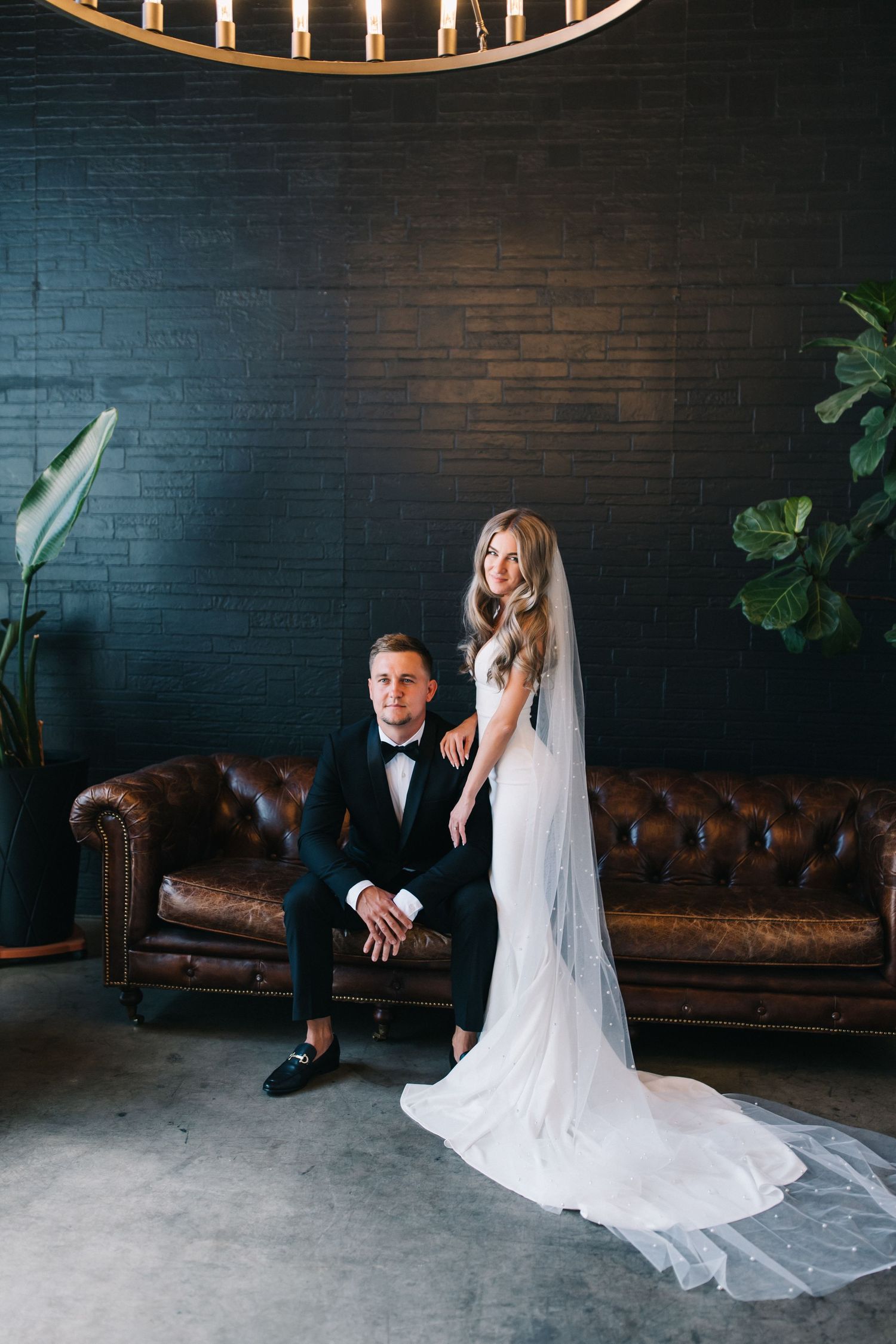 Elegant wedding portrait with a chesterfield sofa and circular chandelier overhead.
