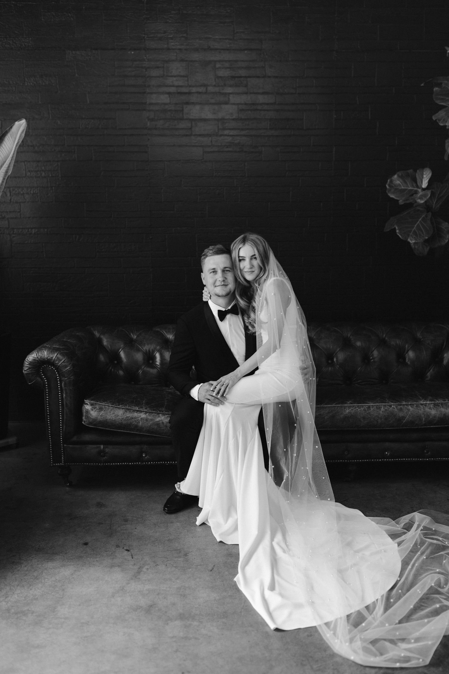 Black and white portrait of newlyweds on a tufted leather sofa.