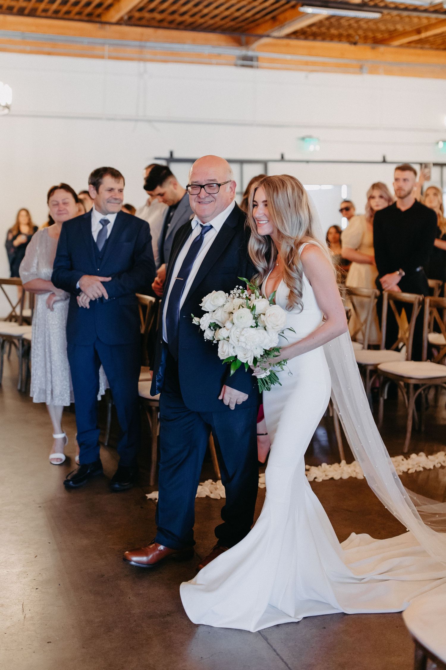 Bride in white gown walks down the aisle with bouquet during wedding ceremony.
