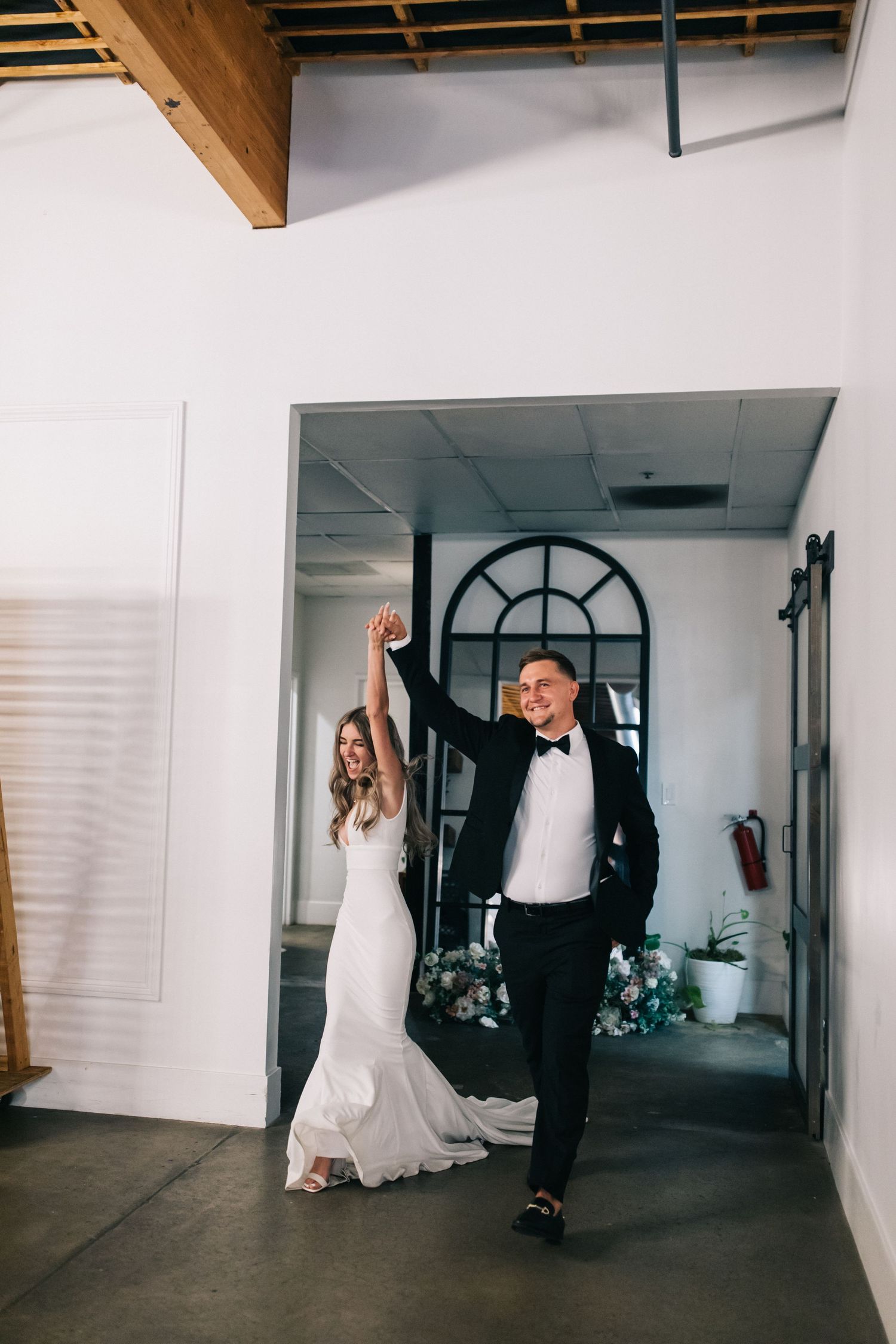 Wedding couple makes grand entrance into modern industrial venue with arched doorway.