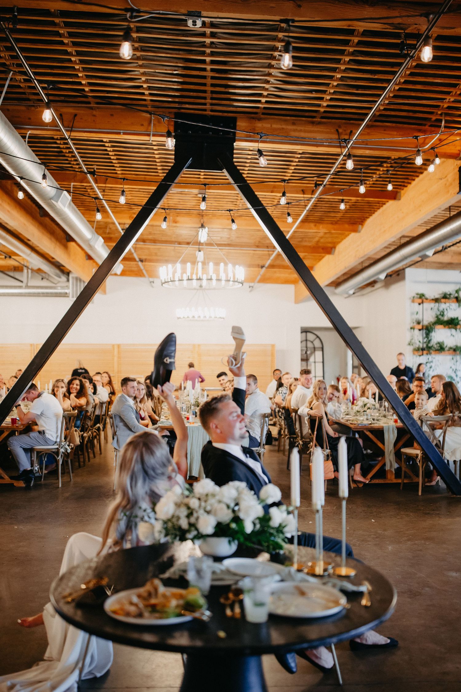 Wedding reception venue with triangular wooden arch and guests seated at tables under string lights.
