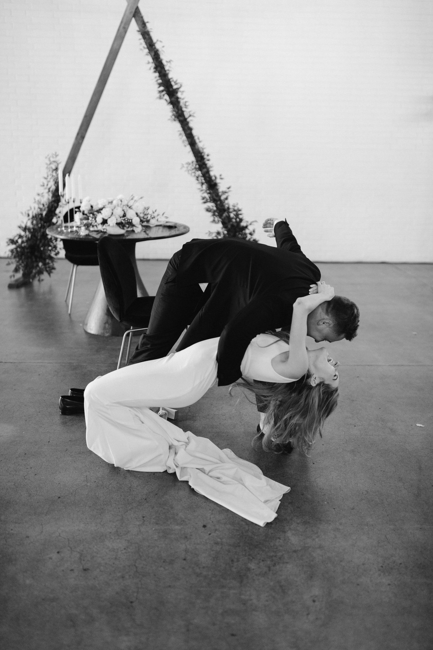 Dramatic black and white photo of wedding couple's dip dance pose under geometric arch.