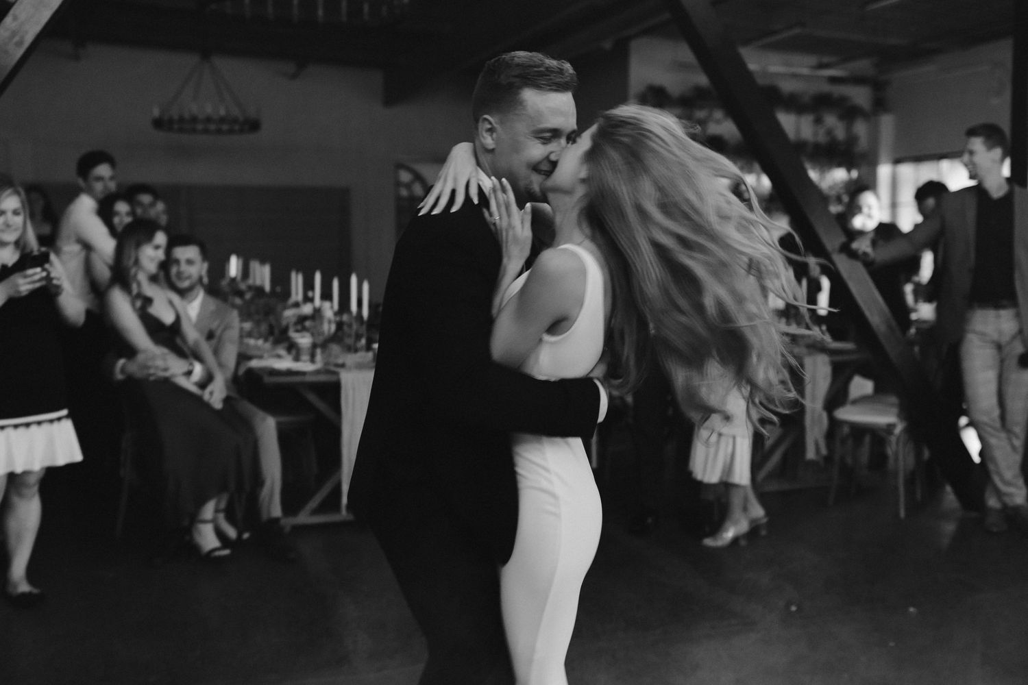 Couple sharing romantic dance moment at wedding reception with guests looking on.
