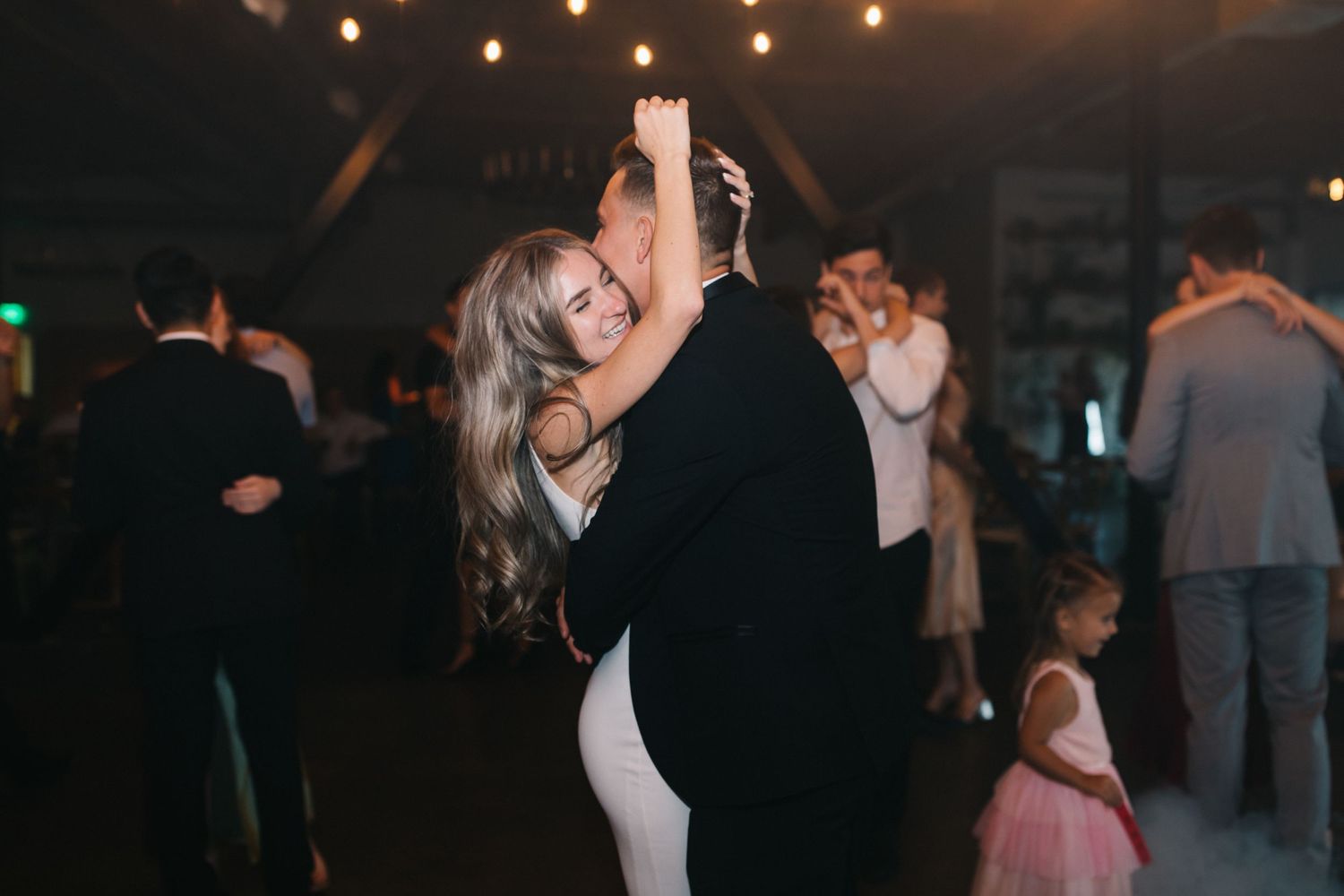 Elegant couple shares an intimate dance together under warm string lights at an evening reception.