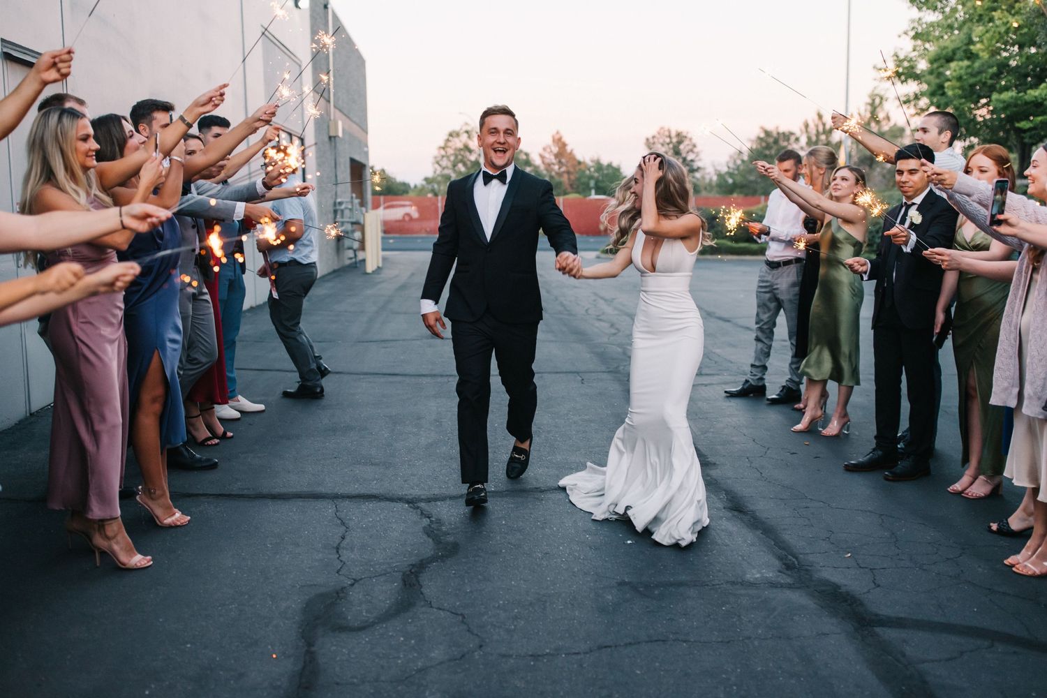 Wedding guests line a path as newlyweds make their grand exit along an outdoor walkway.