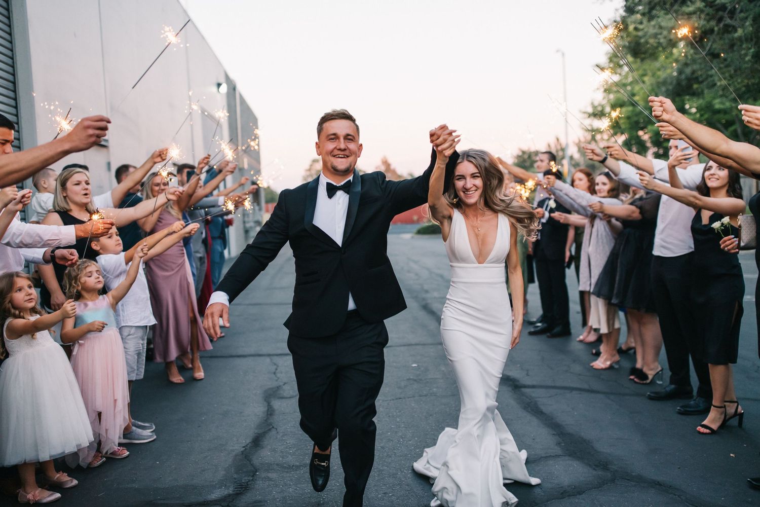 Newlyweds running joyfully through a sparkler exit line formed by wedding guests.