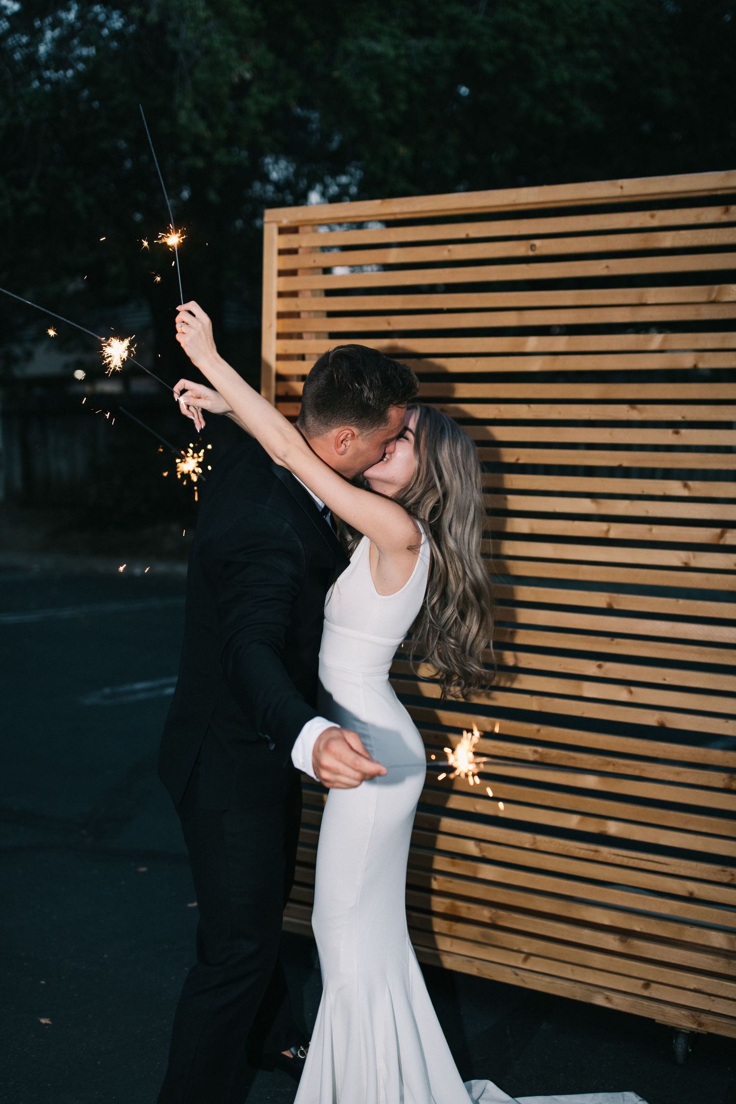 Wedding couple shares romantic sparkler moment against horizontal wood panel wall.