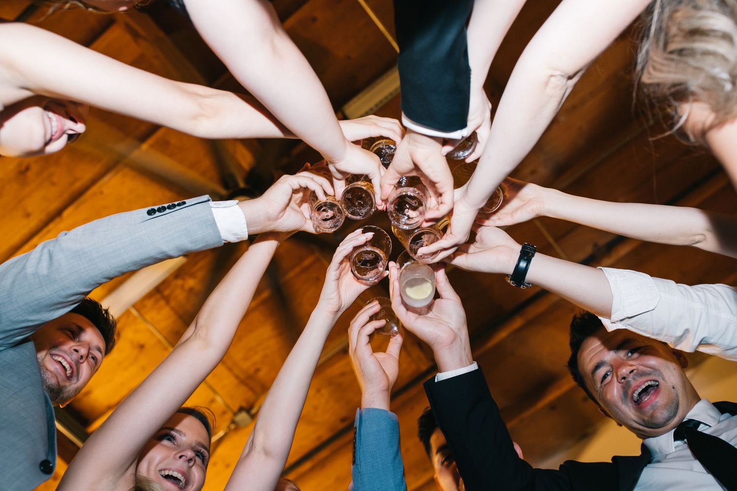 Group of friends raising their hands together in a celebratory toast circle formation.