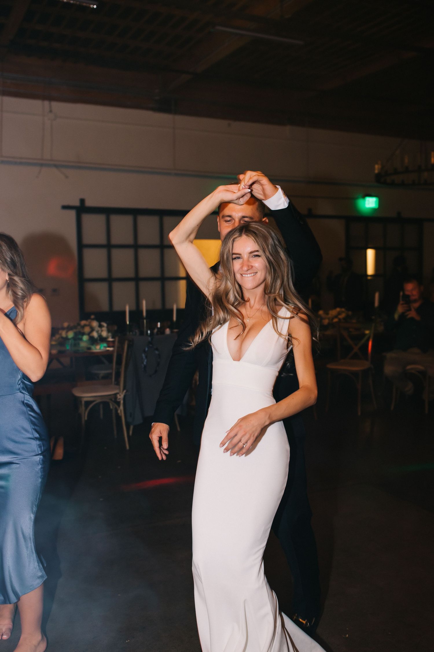 Woman in flowing white gown dances joyfully at an evening celebration under ambient lighting.