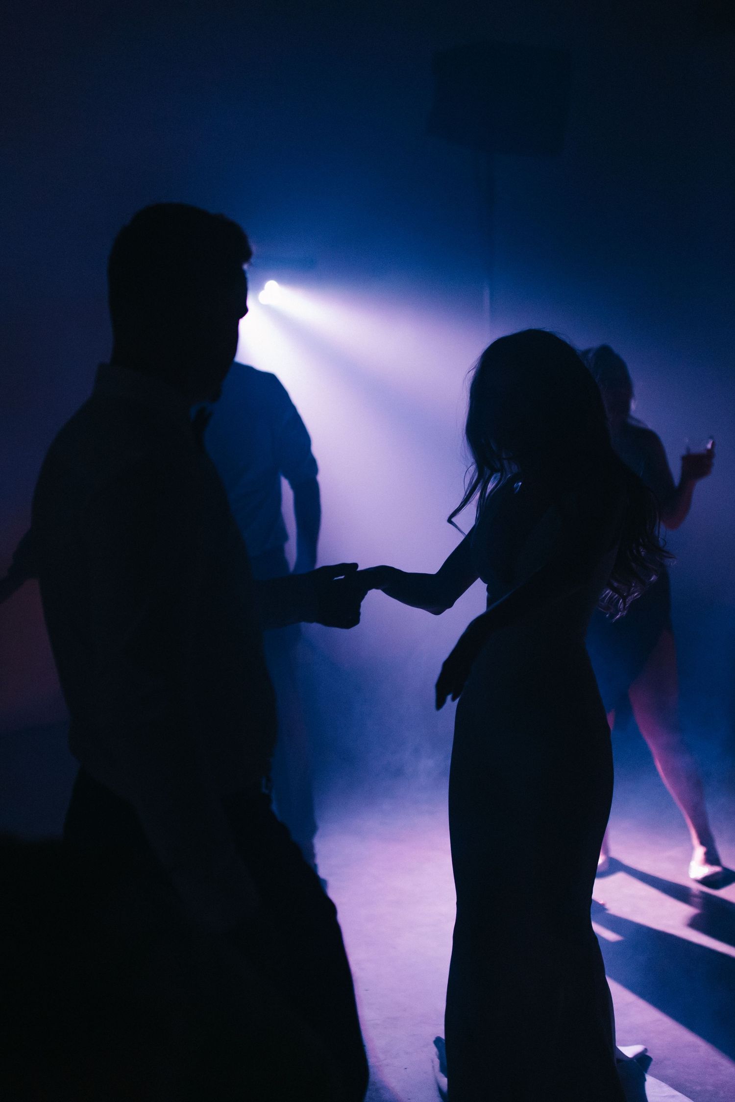 Silhouetted figures dance against dramatic blue lighting at evening celebration.