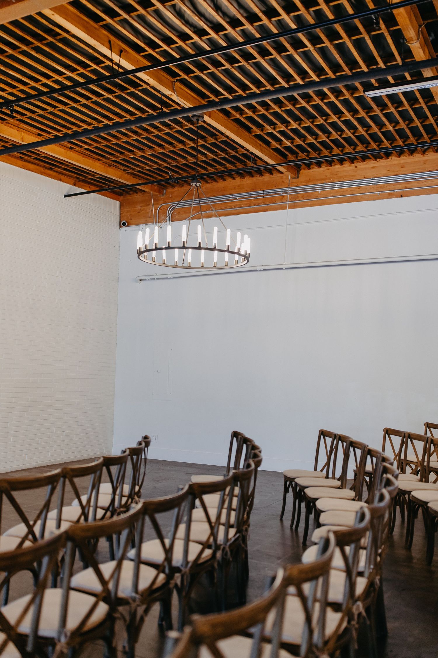 Modern event space with wooden ceiling beams and circular chandelier.