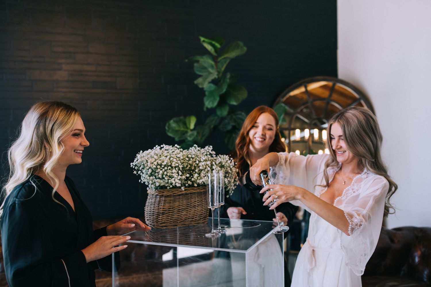 Three friends toasting with champagne glasses near floral arrangement.