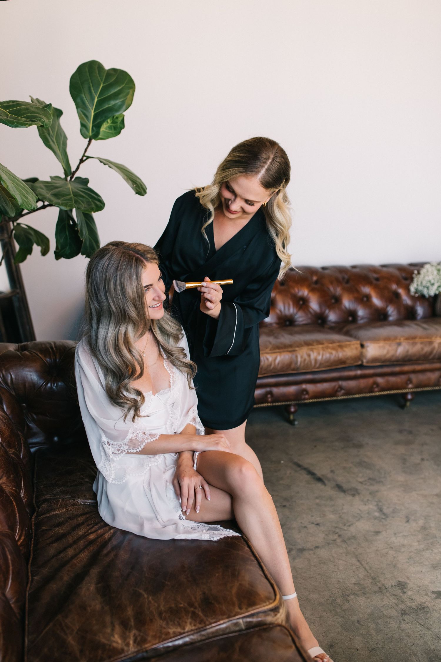 Wedding preparation scene in modern room with leather couch and fiddle leaf fig plant.