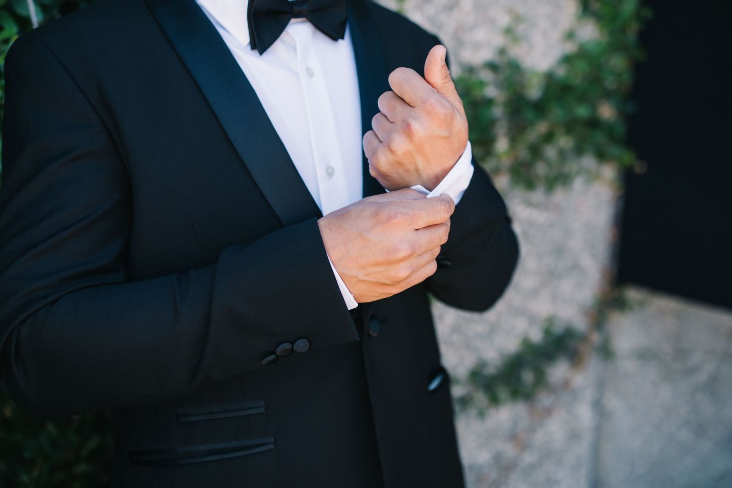 Close-up of hands adjusting cufflinks on black tuxedo sleeve.