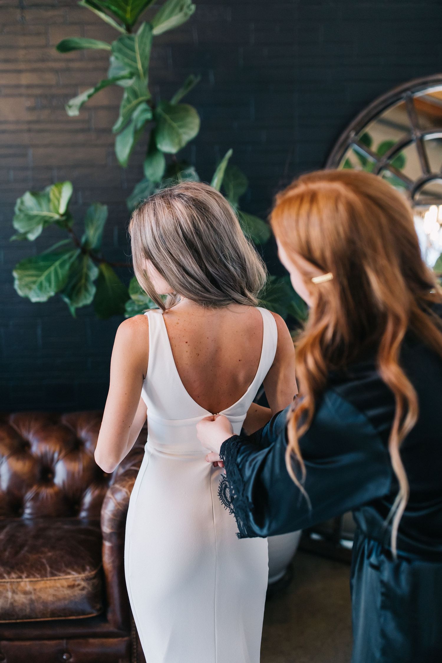 Woman in white dress getting assistance with dress fitting in industrial-style room.