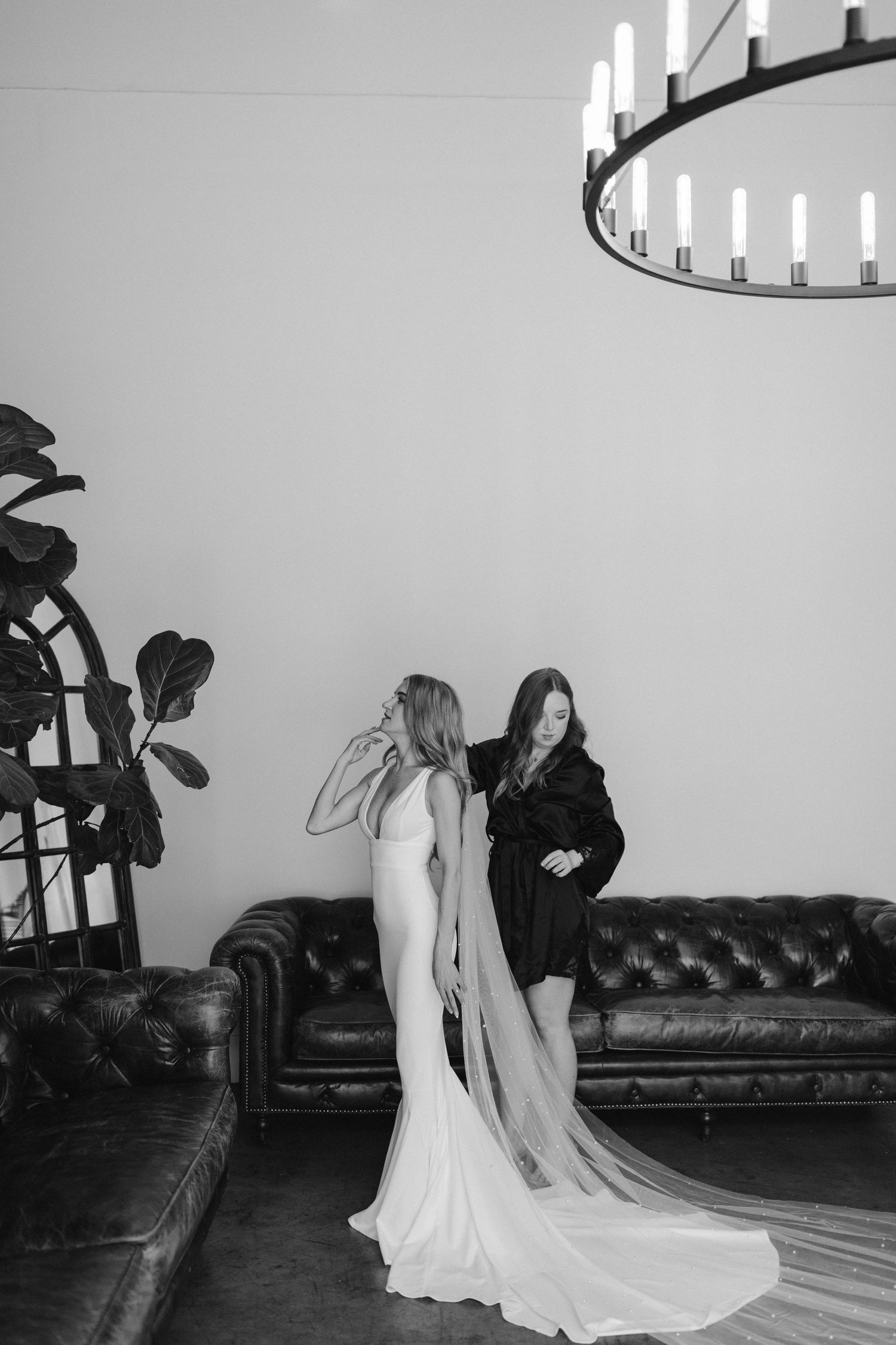 A wedding scene with a flowing white gown and black dress against a brown leather couch.