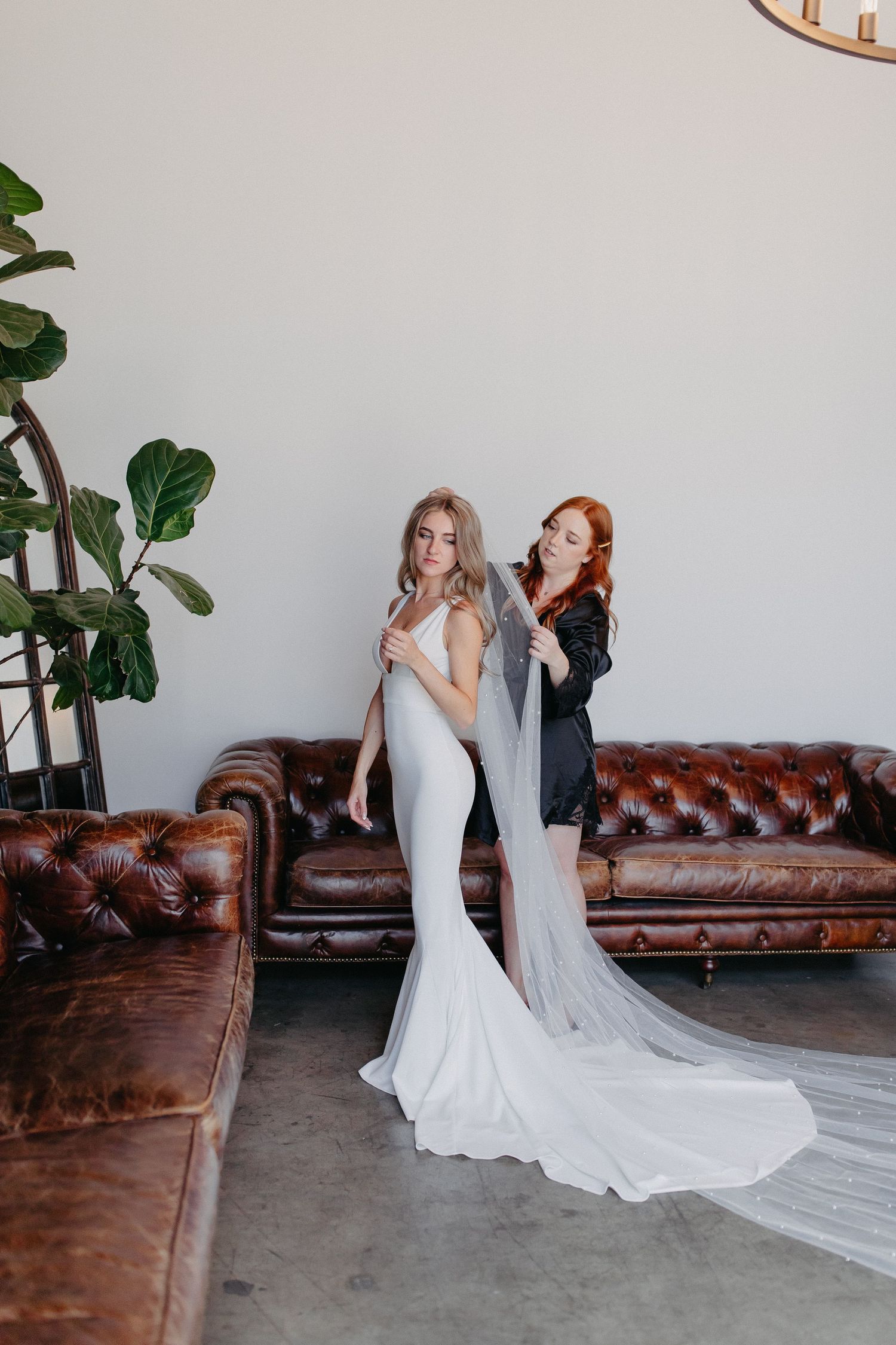 A bridal preparation scene with a white fitted wedding gown and veil against a leather couch backdrop.