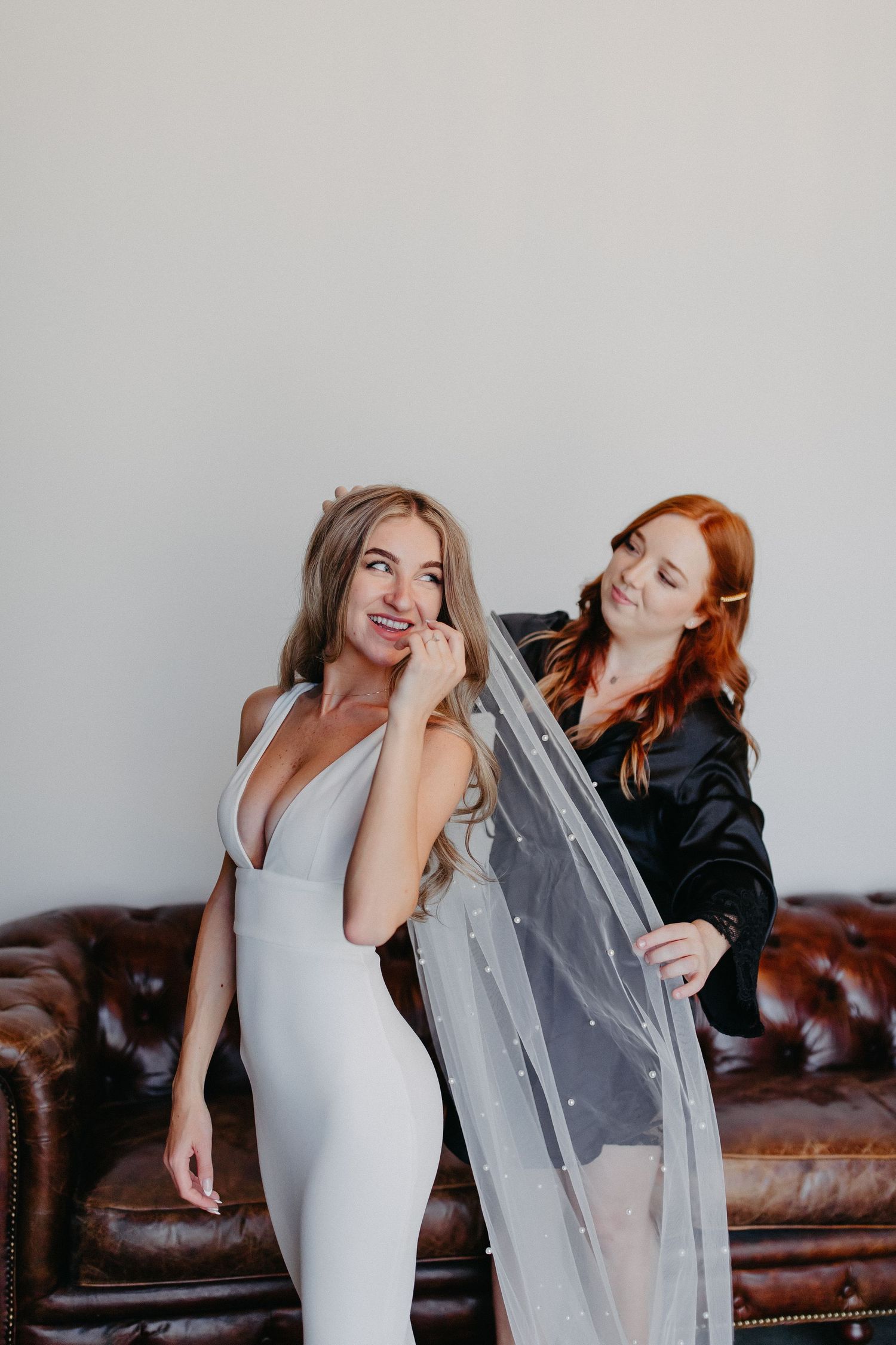 Two people share a playful moment while adjusting a wedding veil in a modern indoor setting.